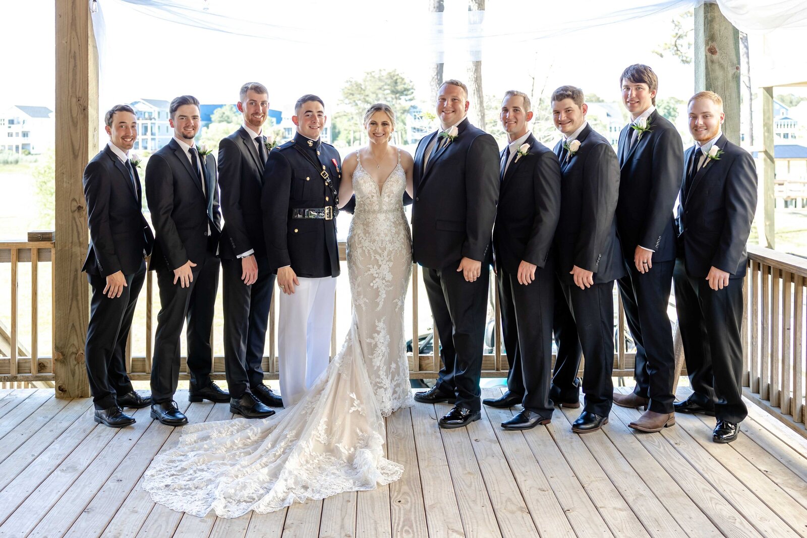 The bride and groom pose with the groomsmen on a wooden deck at an oceanfront wedding venue in Carolina Beach, NC, blending rustic charm with elegant coastal vibes.