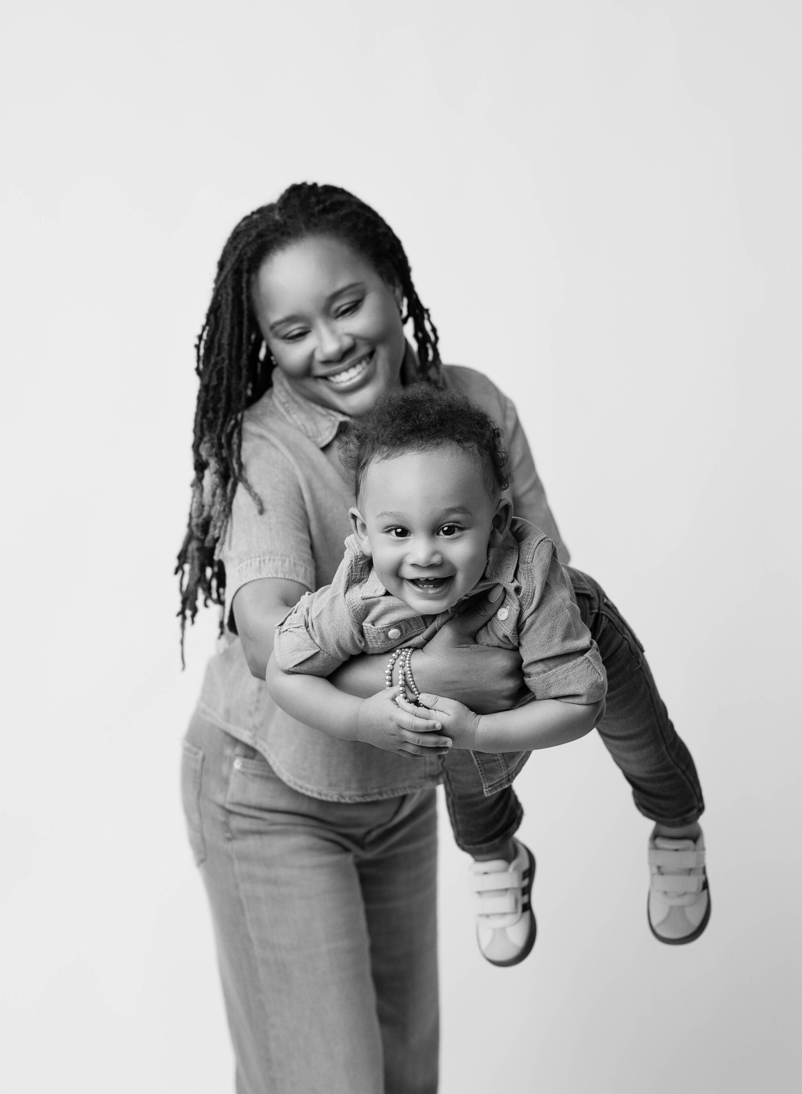 Mom swinging baby boy on white backdrop while taking family photos.