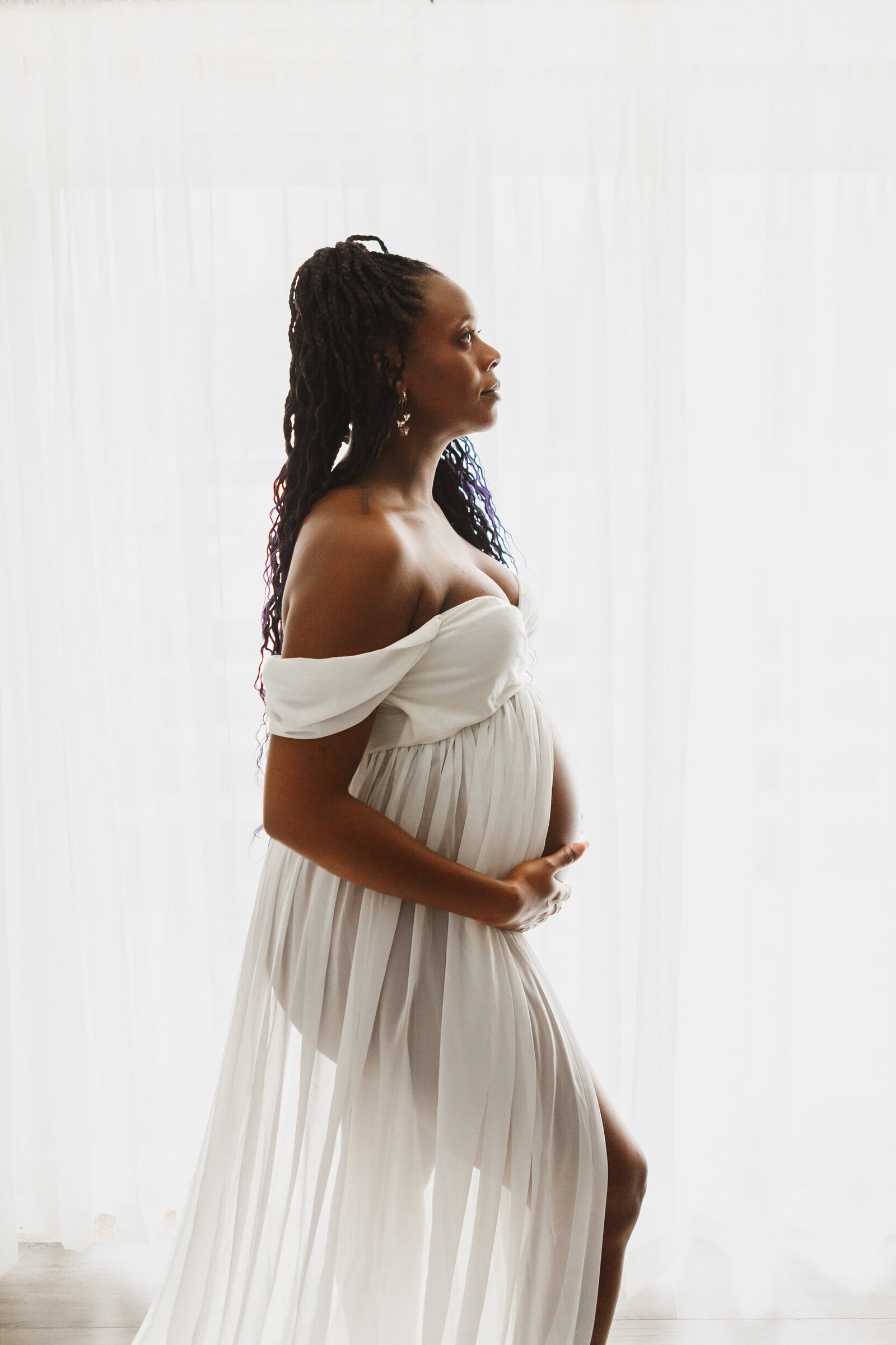 Woman in white dress, backlit holding pregnant belly