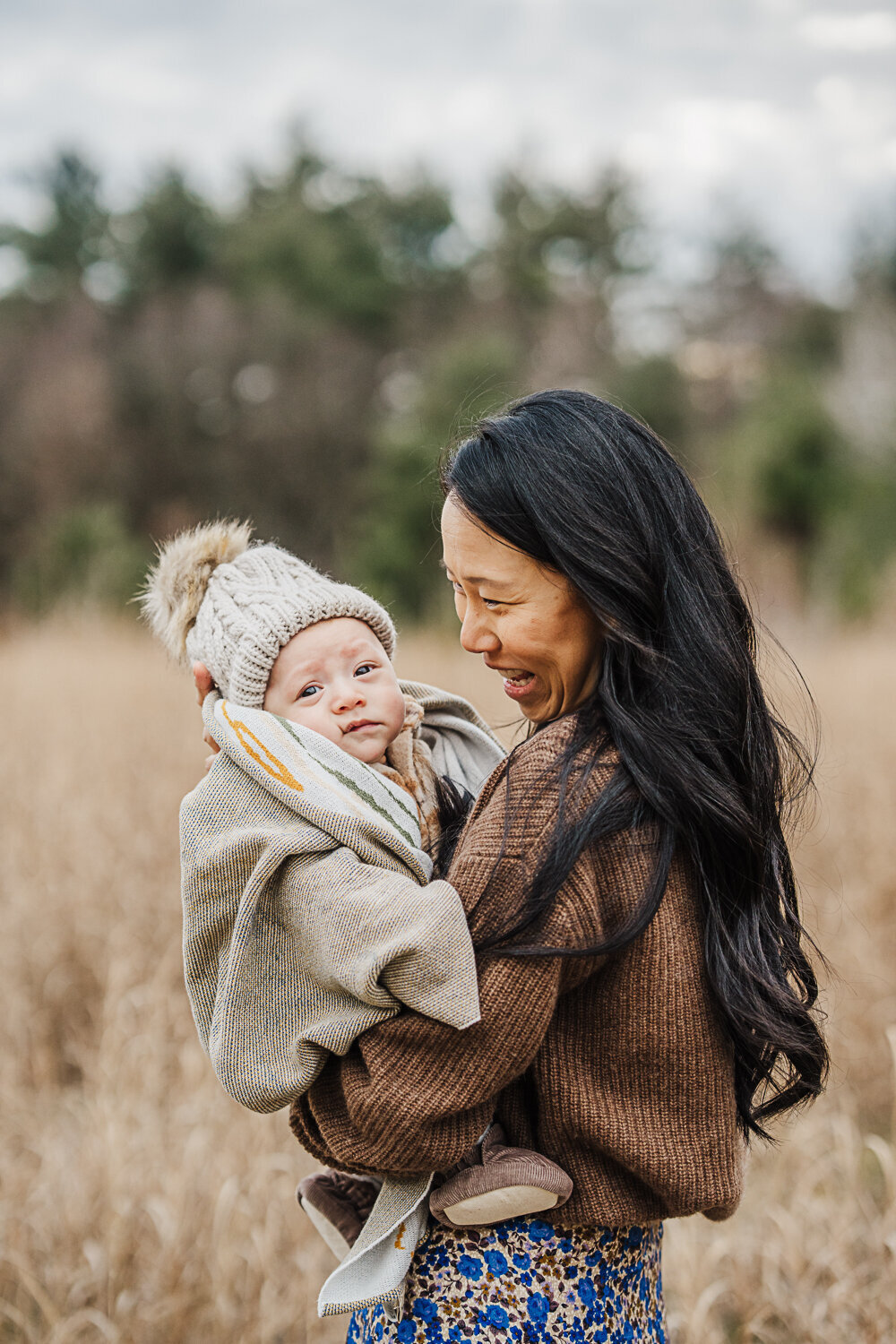 mother holds infant son wrapped in a blanket for winter family photos