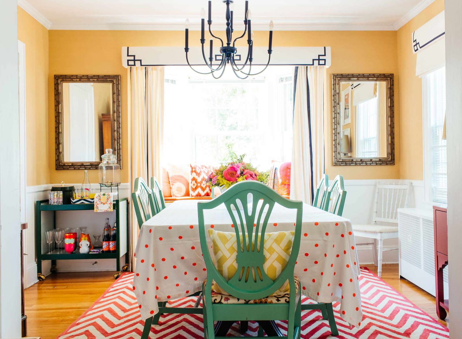 A yellow dining room with green chairs and chevron rug.