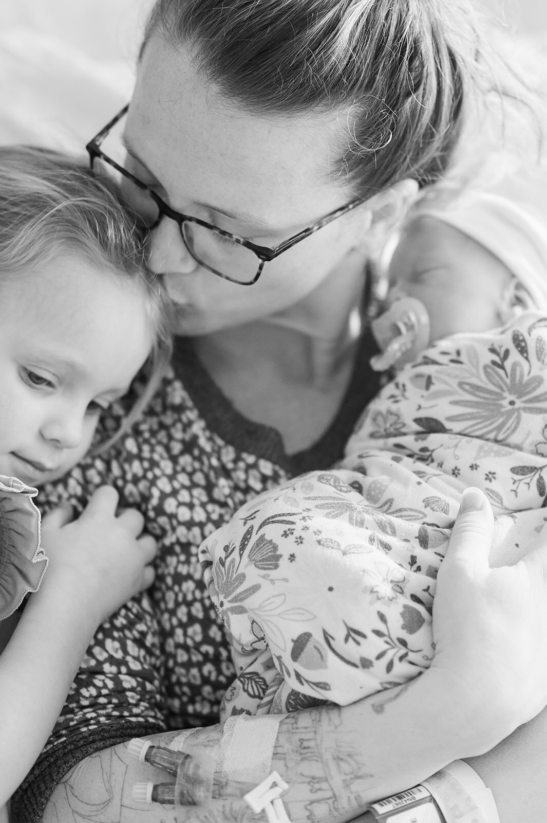 Black and white photo of mom holding toddler and a newborn baby in hospital