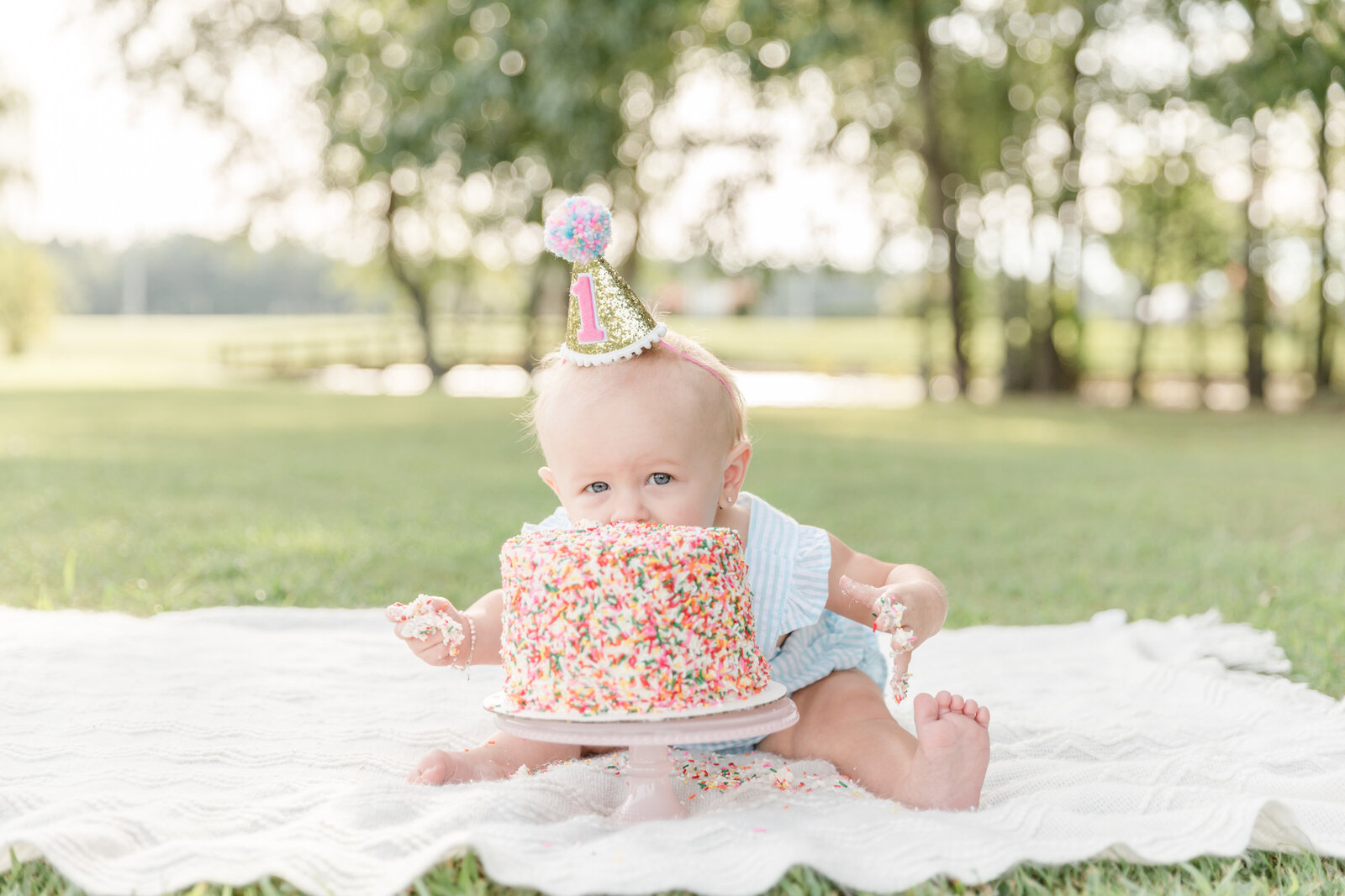 Baby with face in a sprinkle covered first birthday cake.