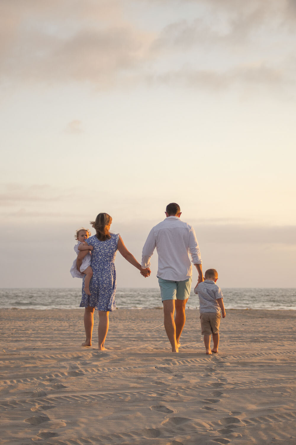 Family of four walking hand in hand along the beach at sunset