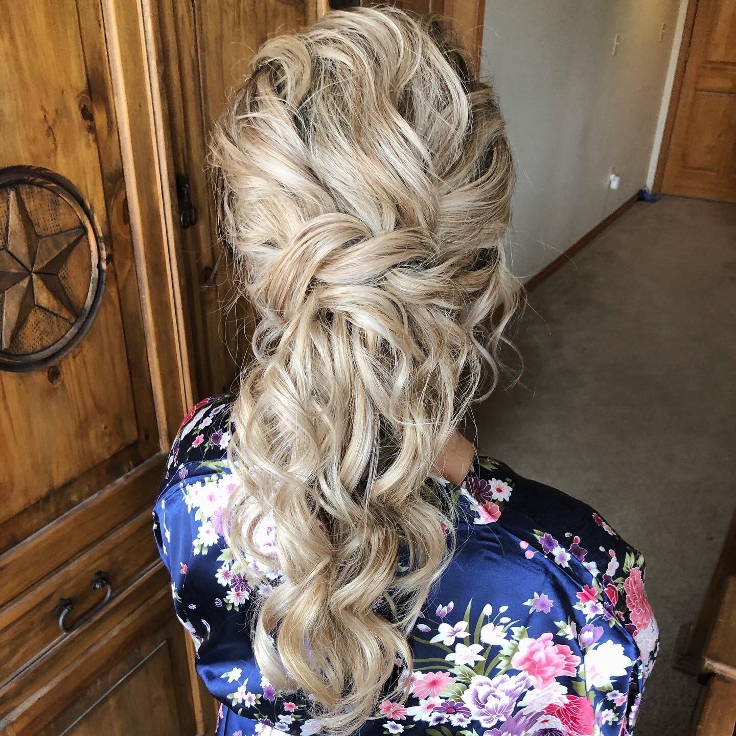 Blonde hair styled in an intricate braided updo, with loose curls, complements the floral-patterned robe. Discover what to expect from a wedding makeup artist during your bridal hair and makeup process, ensuring you walk down the aisle flawlessly.