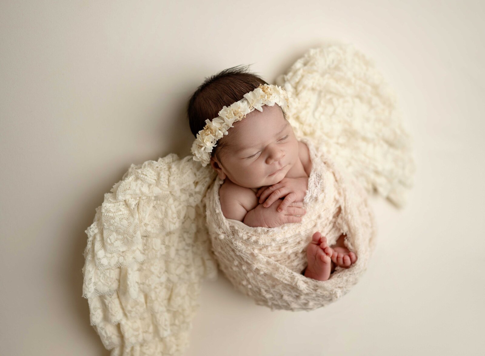 Baby girl in cream swaddled laying on lace angle wings and sleeping. Photographed at Woodstock studio by Atlanta.