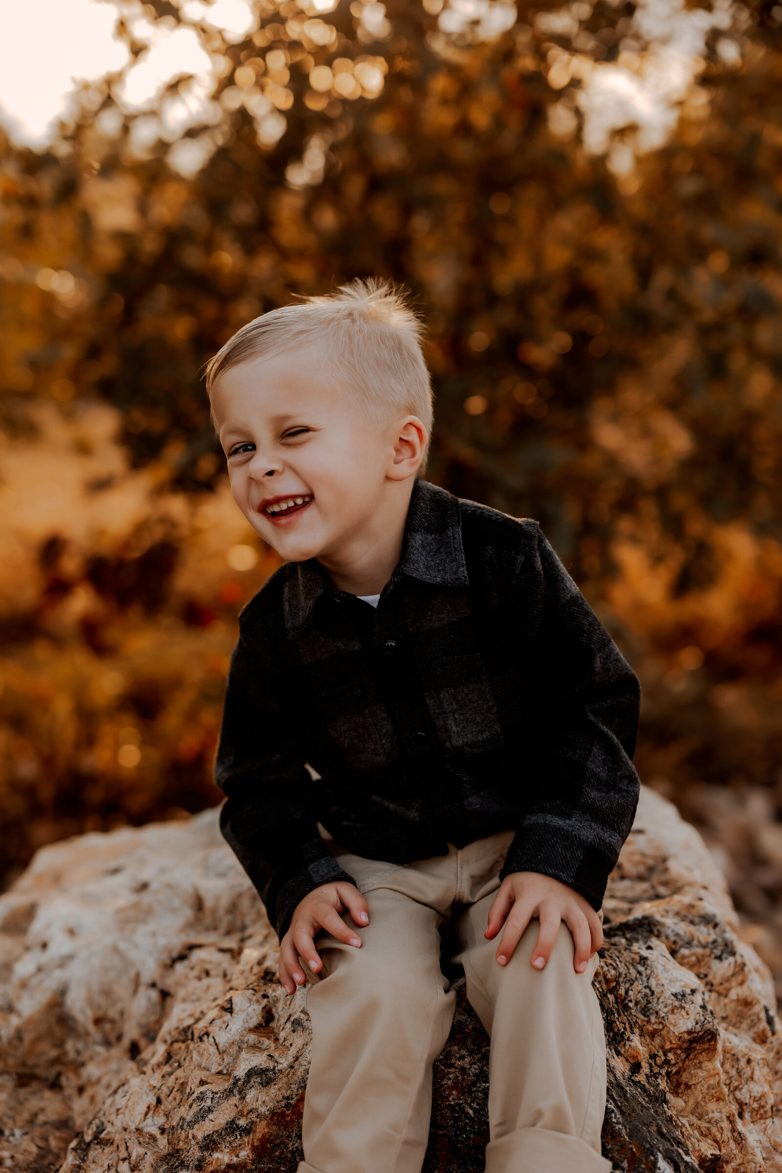 young boy sits on rock winking at camera