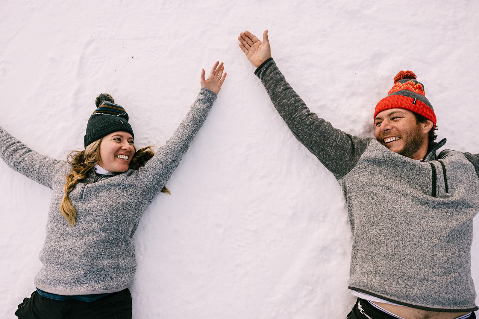 Couple making snow angels on Breckenridge Mountain during engagement photoshoot