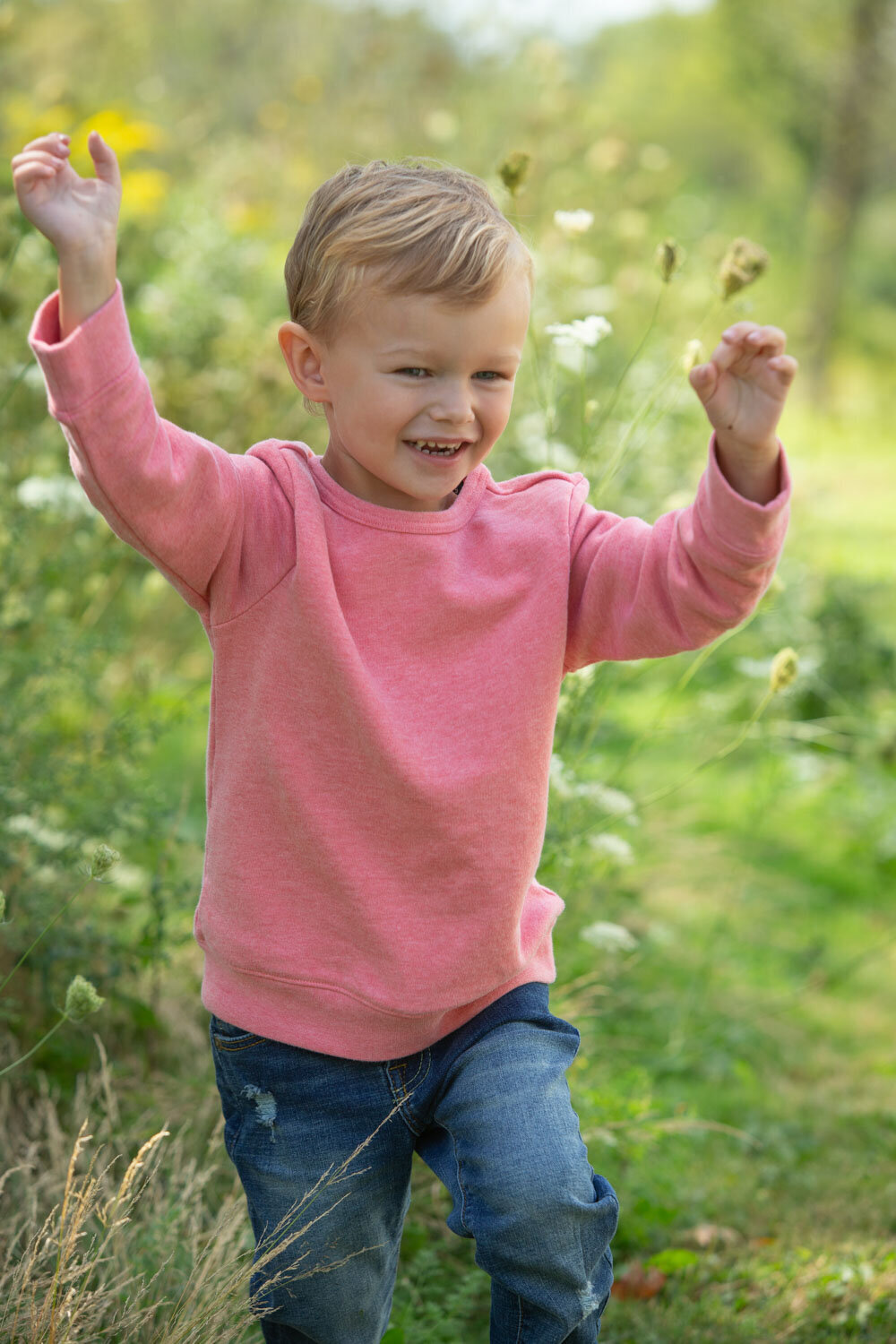 A little boy is wearing a pink sweater and jeans.