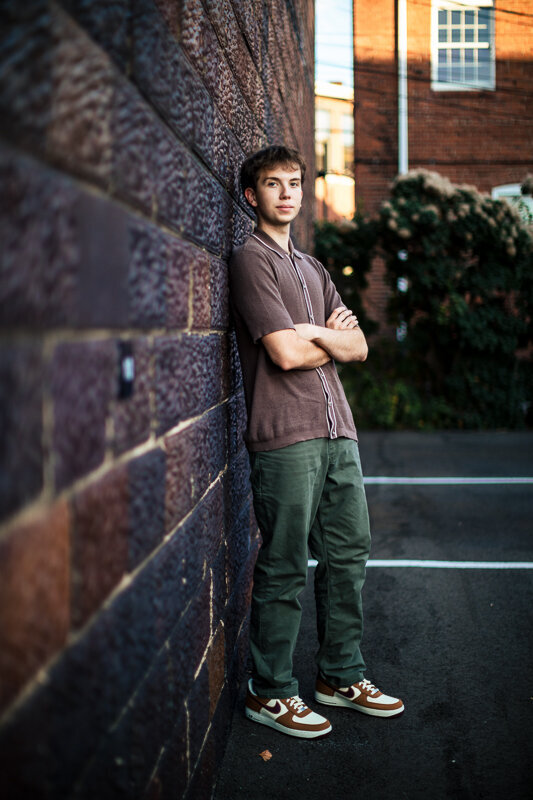 Fall senior session with teen boy leaning against stone wall in park.