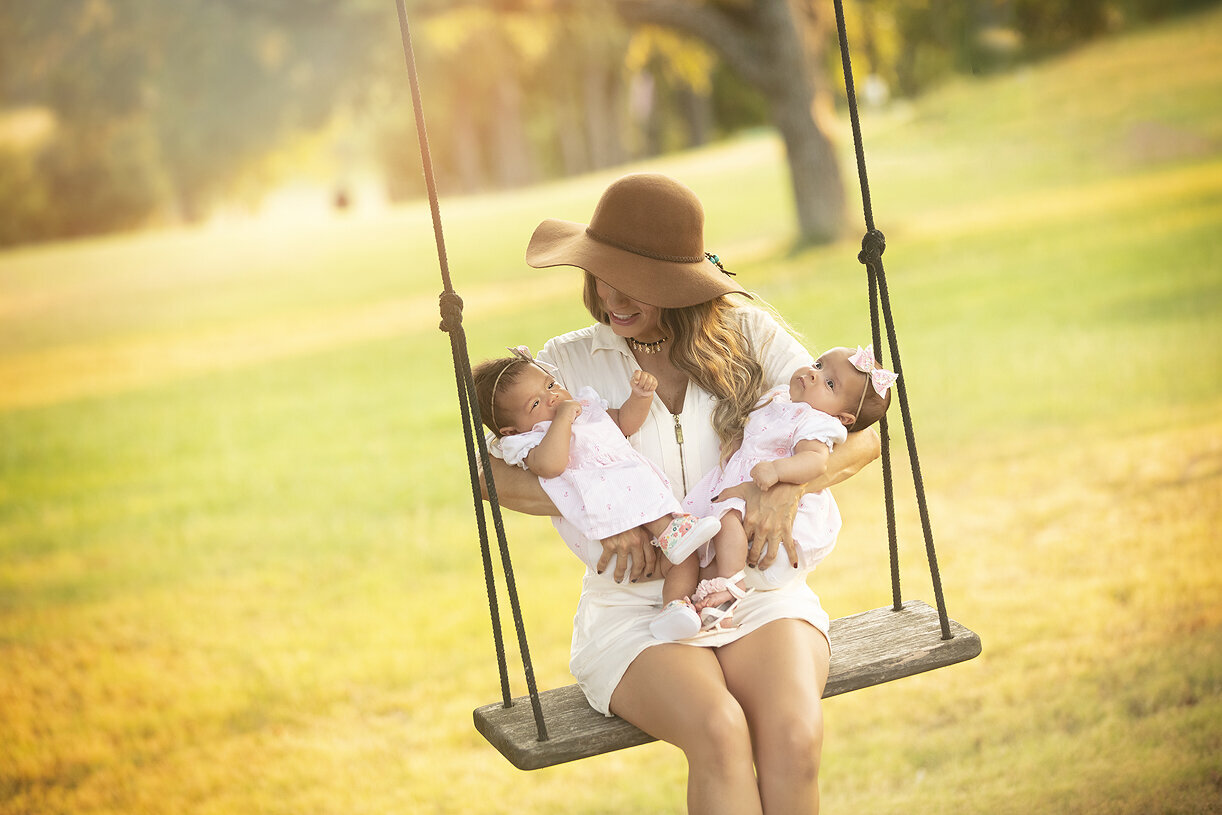 Mother sitting on swing with infant twin daughters