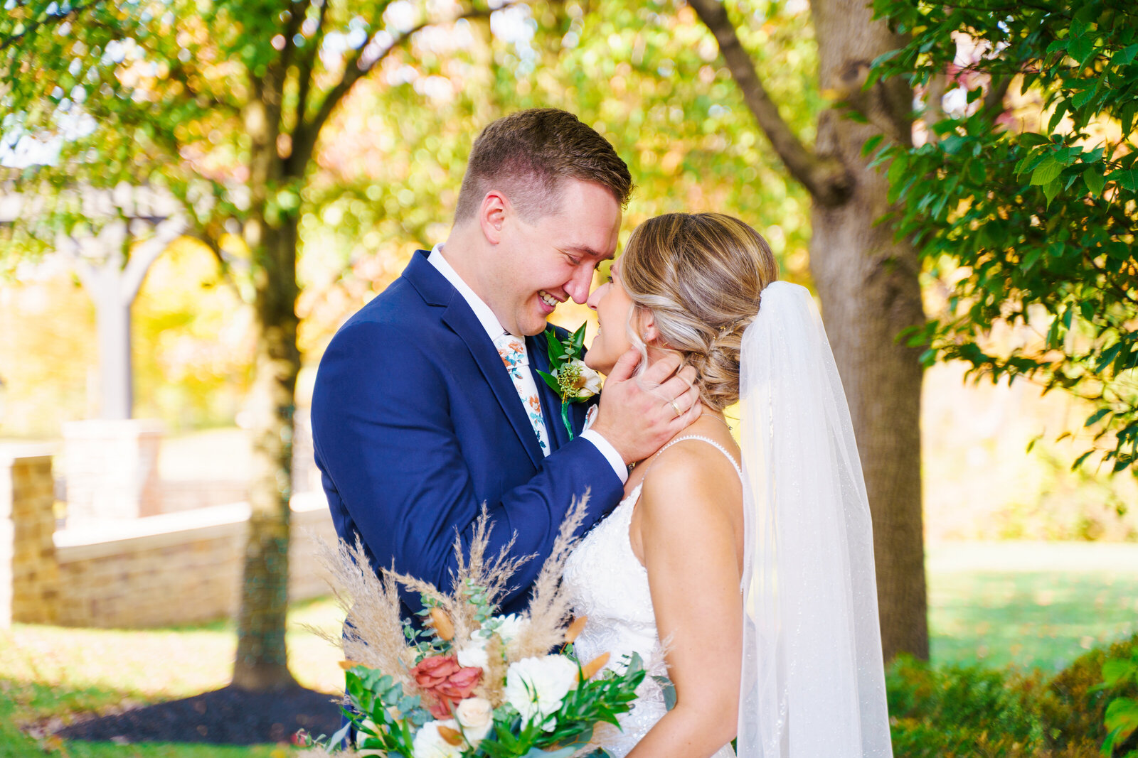 Bride and groom touch foreheads and smile at each other in front of fall foliage at Pinnacle Golf Course in Grove City, Ohio.