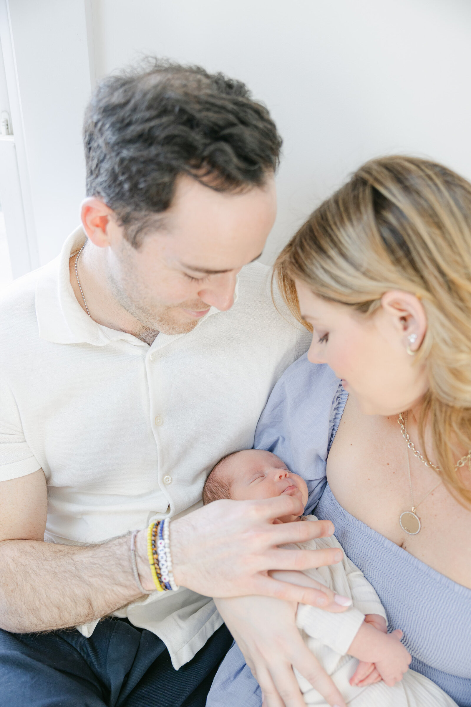 Close-up of a new family cuddling their newborn during an in-home newborn session in Fairfield County, CT. Captured by Nicole Neira Photography, this intimate moment highlights soft lighting, gentle expressions, and a calming pastel colour palette that reflects a cozy lifestyle photography experience.