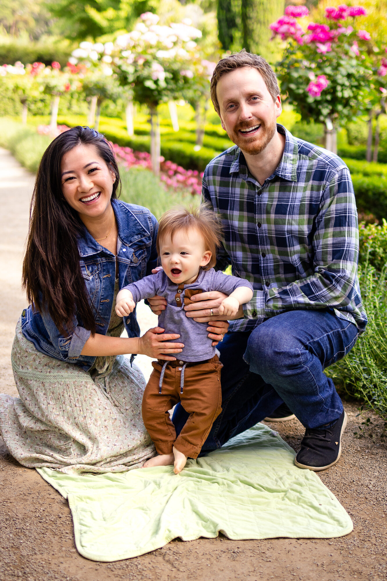 A family beams with joy during a playful garden photo session, beautifully framed by Ellobelle Photography.