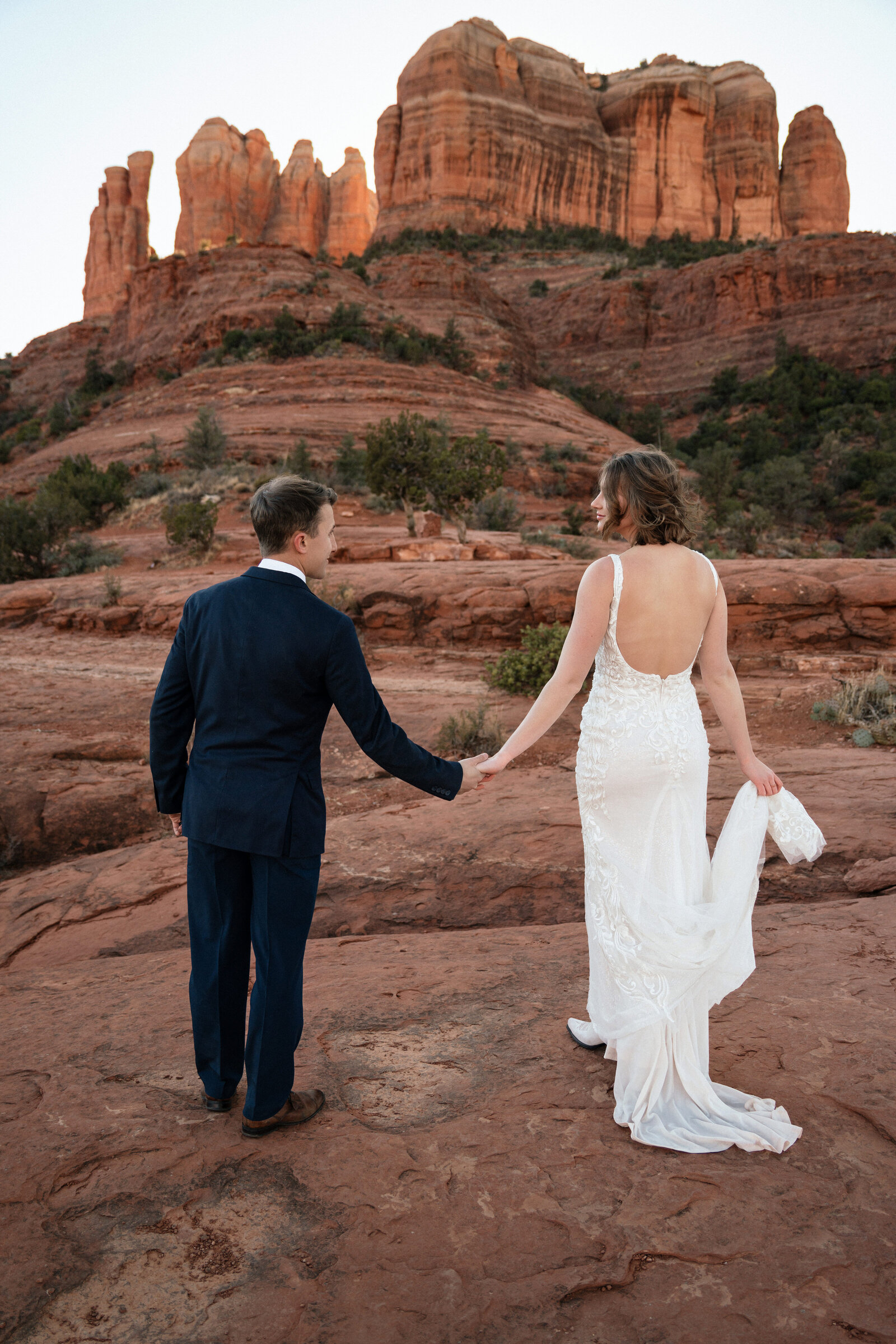 Bride and groom embracing during their sunset elopement at Cathedral Rock in Sedona, Arizona, surrounded by iconic red rock formations and golden light.
