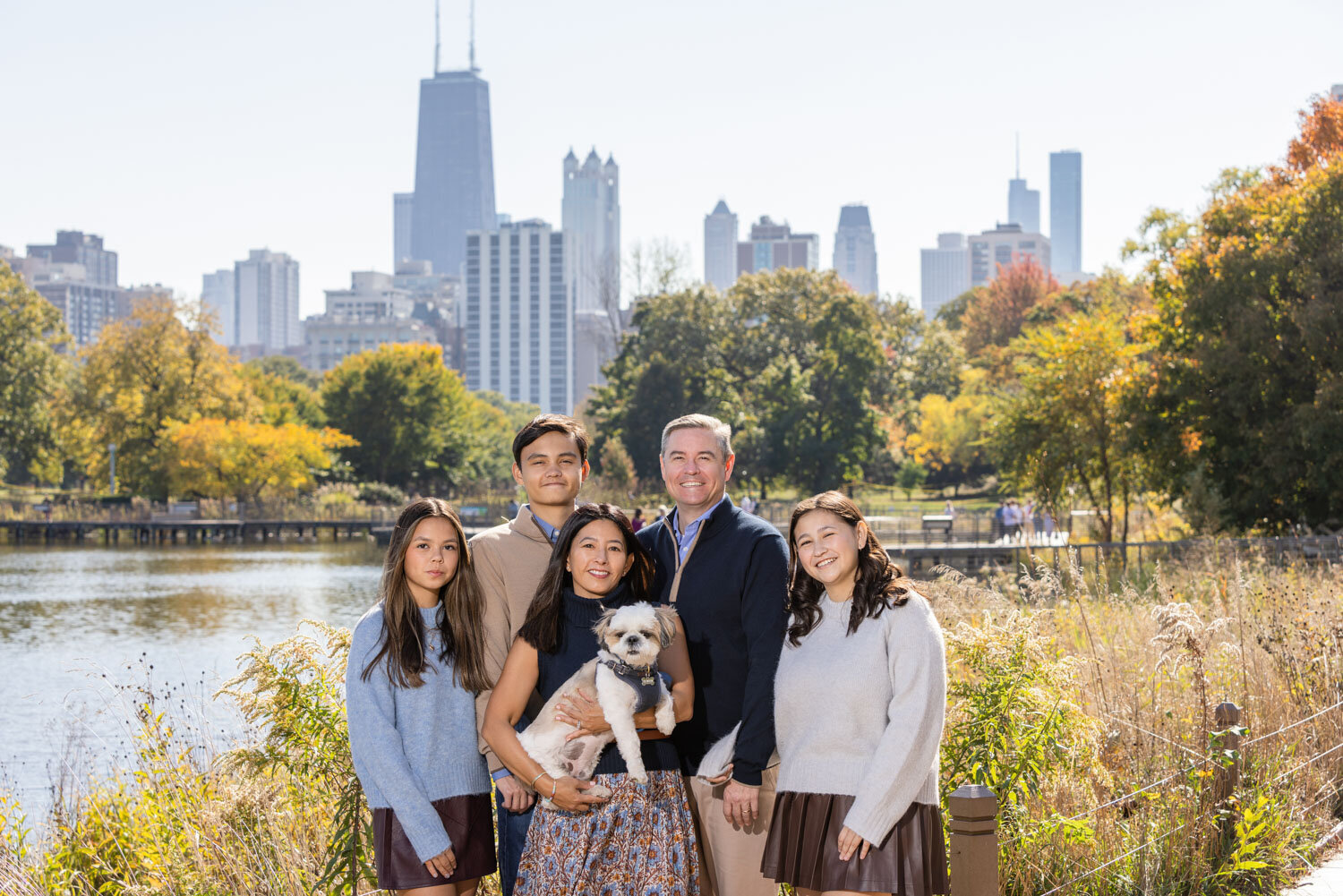 Family portrait with their puppy with greenery and tall buildings behind
