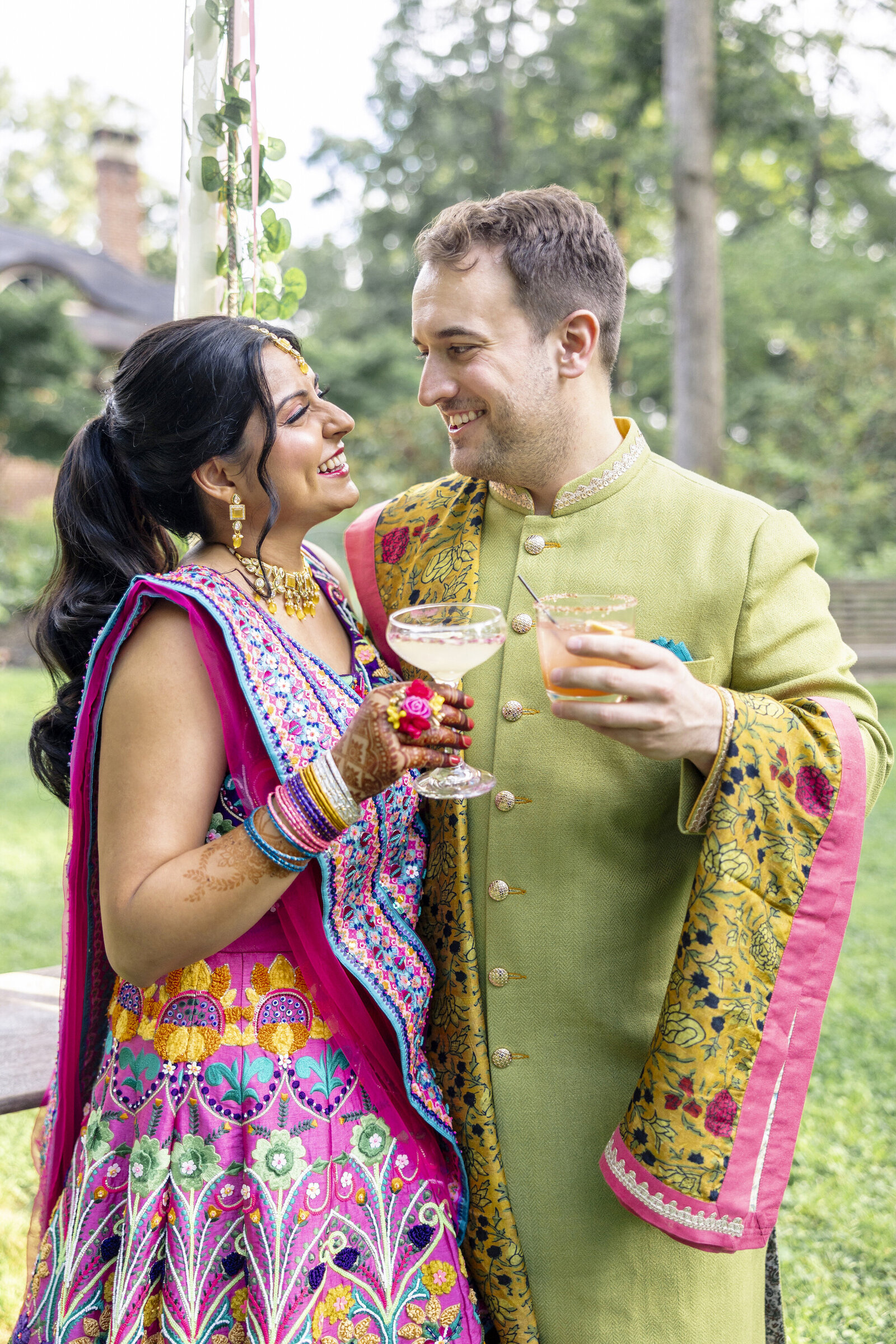 Bride and groom are smiling at each other while holding cocktails at Sangeet in Gramercy Mansion Gardens.