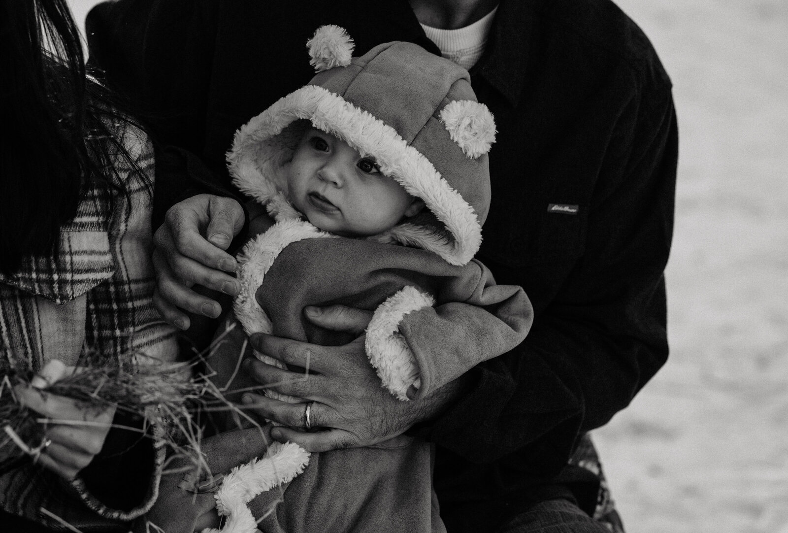 Bundled up baby is held by parents during their winter family photo session in Lee, New Hampshire