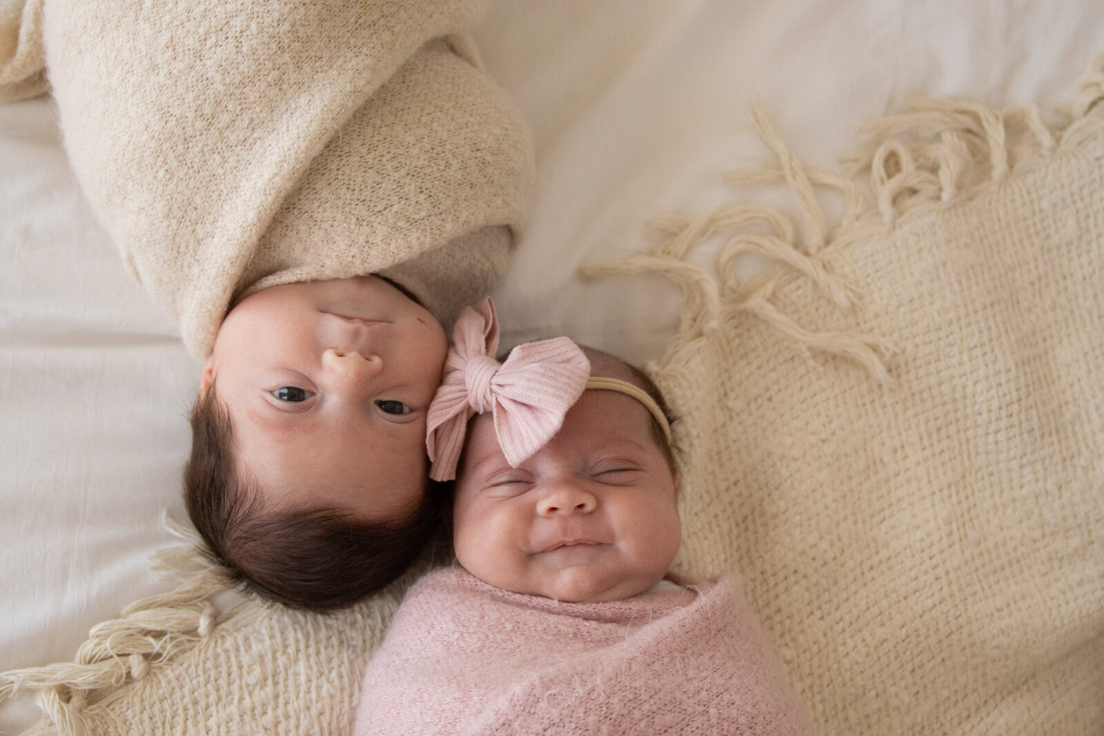twins swaddled on bed facing opposite directions looking up at the camera