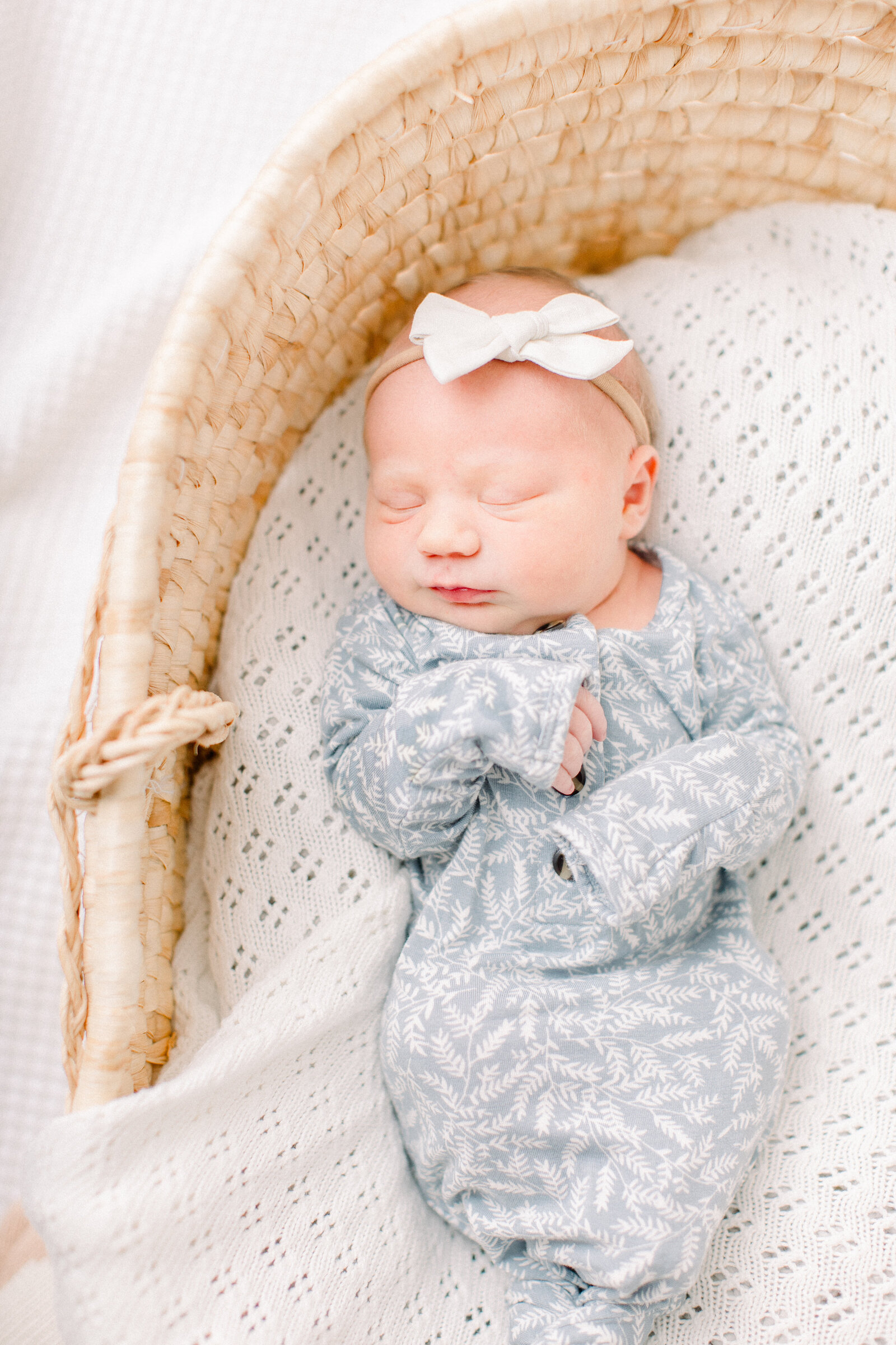Baby sleeping soundly in a blue and white Lou Lou & Co knotted onesie on a white crochet blanket in a moses basket by NH newborn photographer Fieldstone Studio.
