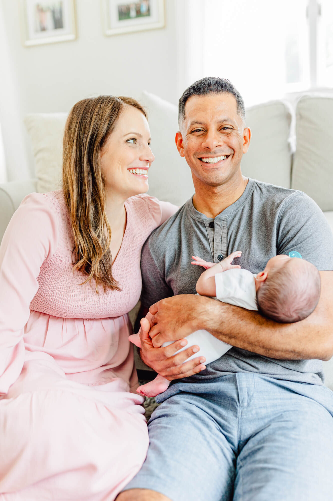 Dad smiles and holds his newborn while mom smiles at dad