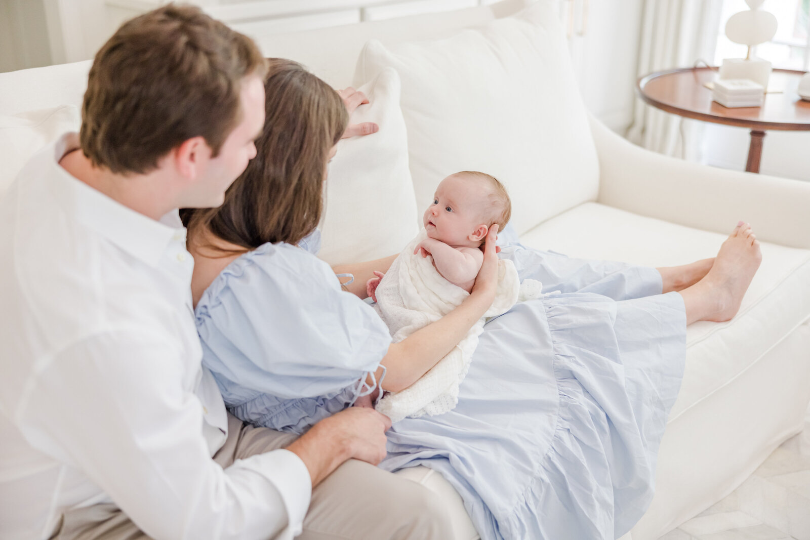 Parents seated on a couch with a newborn in their arms.