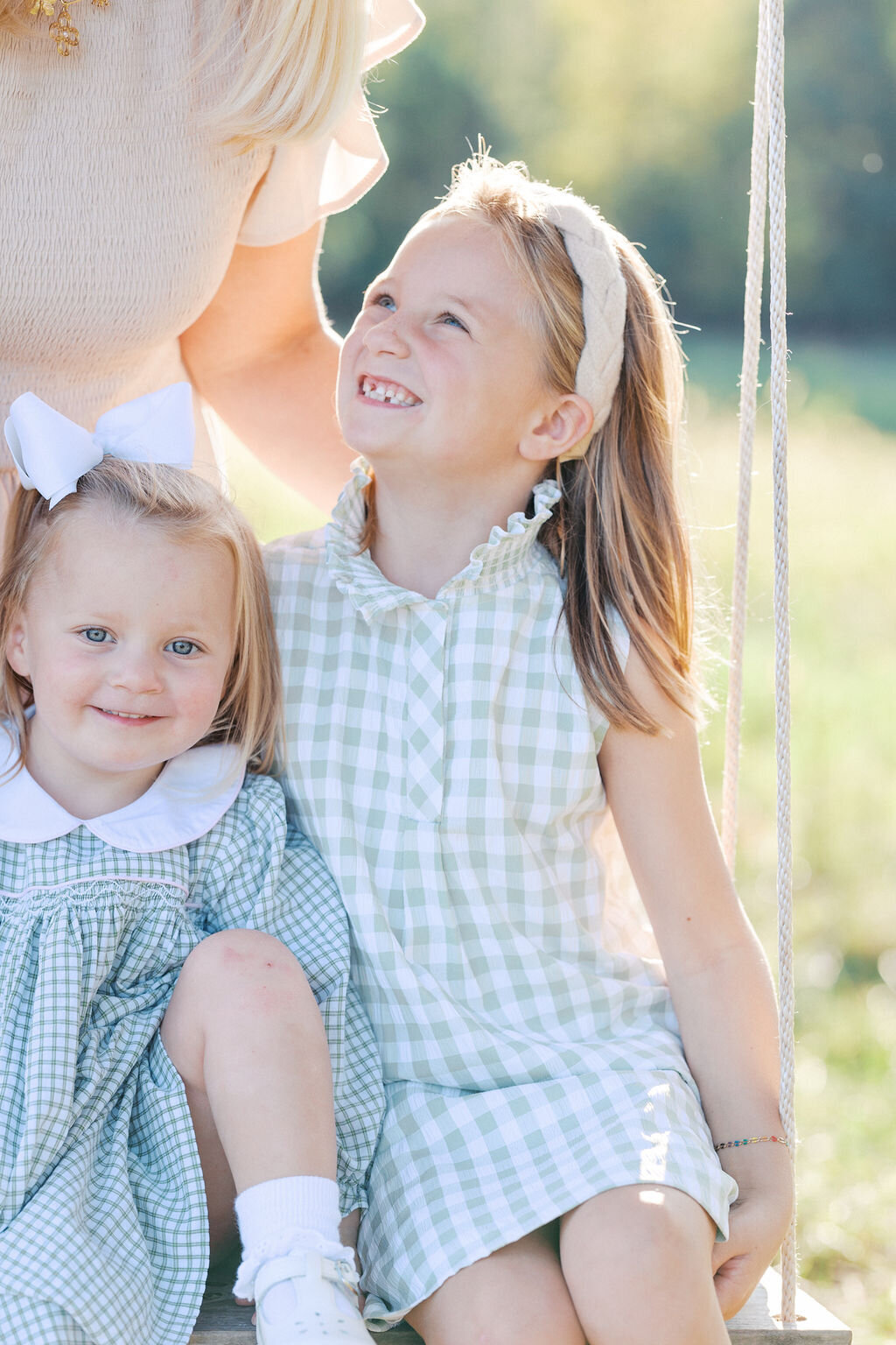 two girls in green gingham dresses smile up at their mother