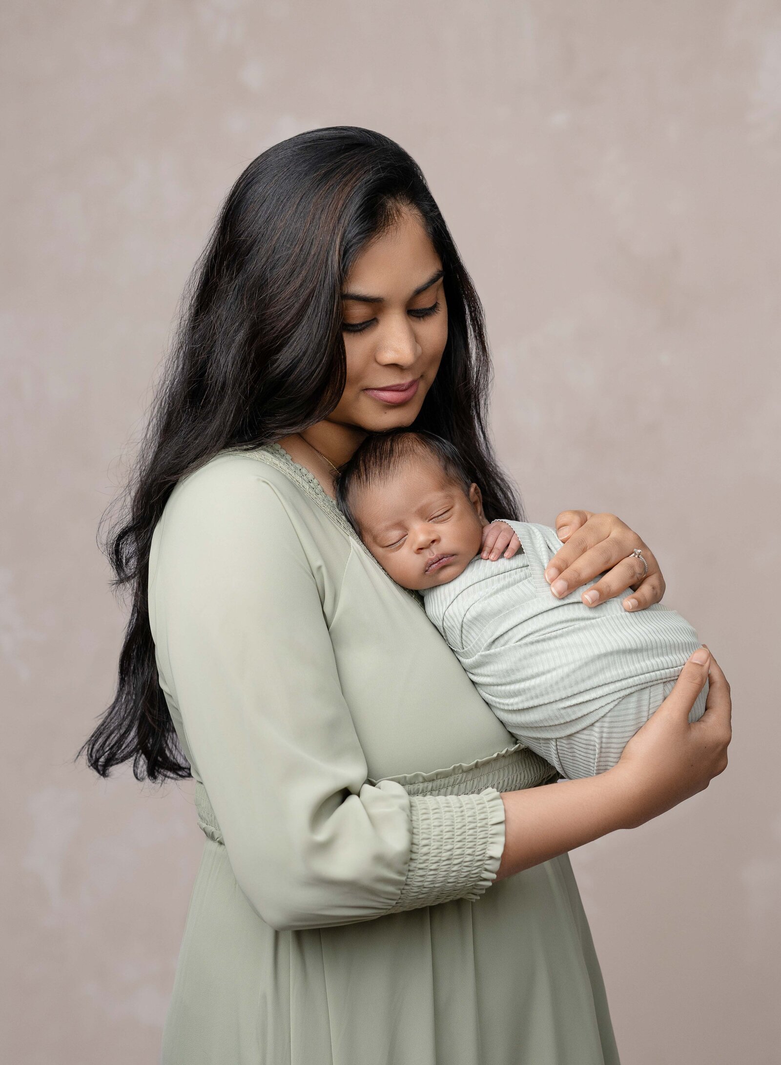 Baby in sage swaddled and sleeping on Mom's chest. Newborn Photography session photographed at Jenni Nikki's photo studio in Marietta, GA.