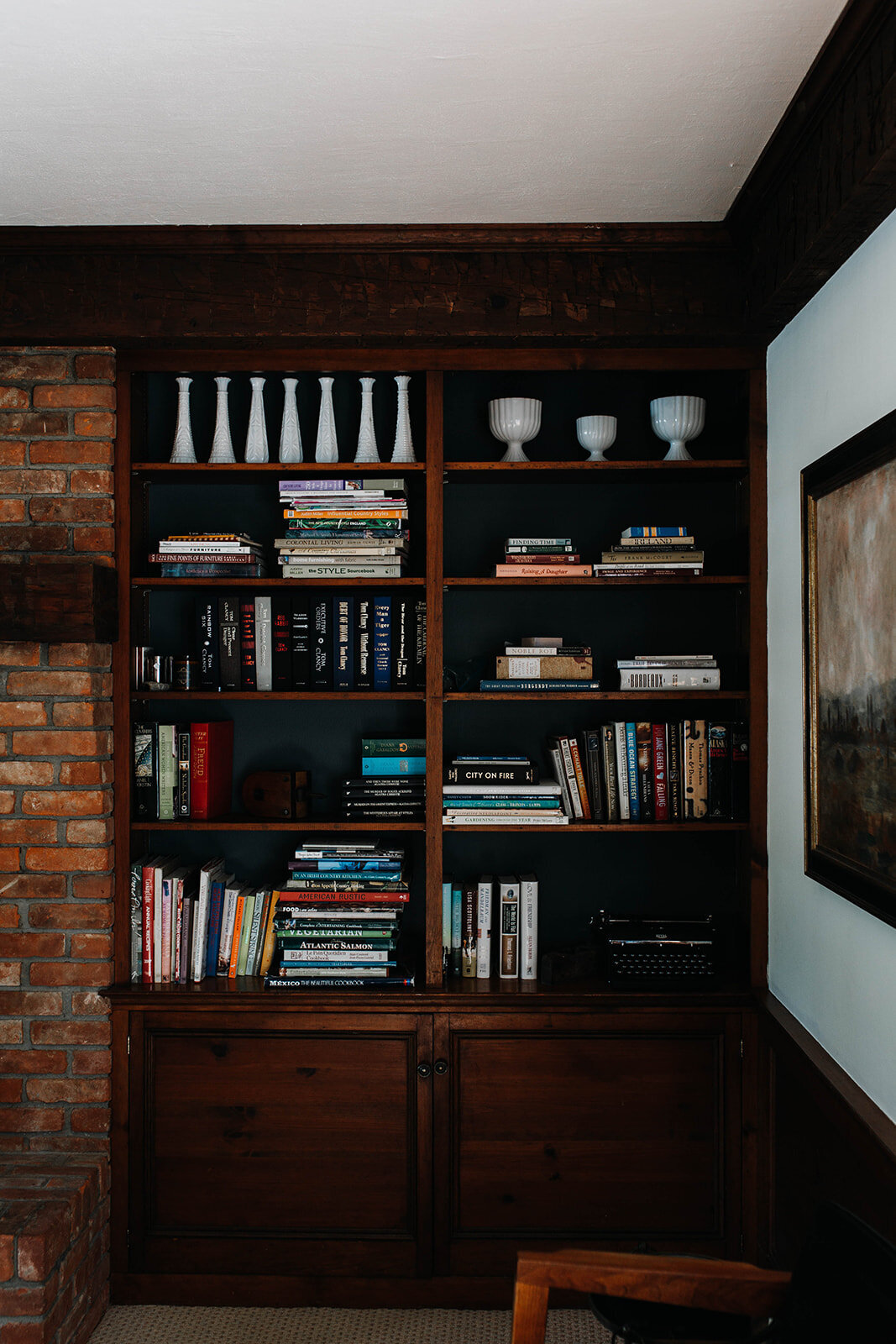 handsome wood bookshelves with navy walls next to a brick fireplace at the farmer cottage