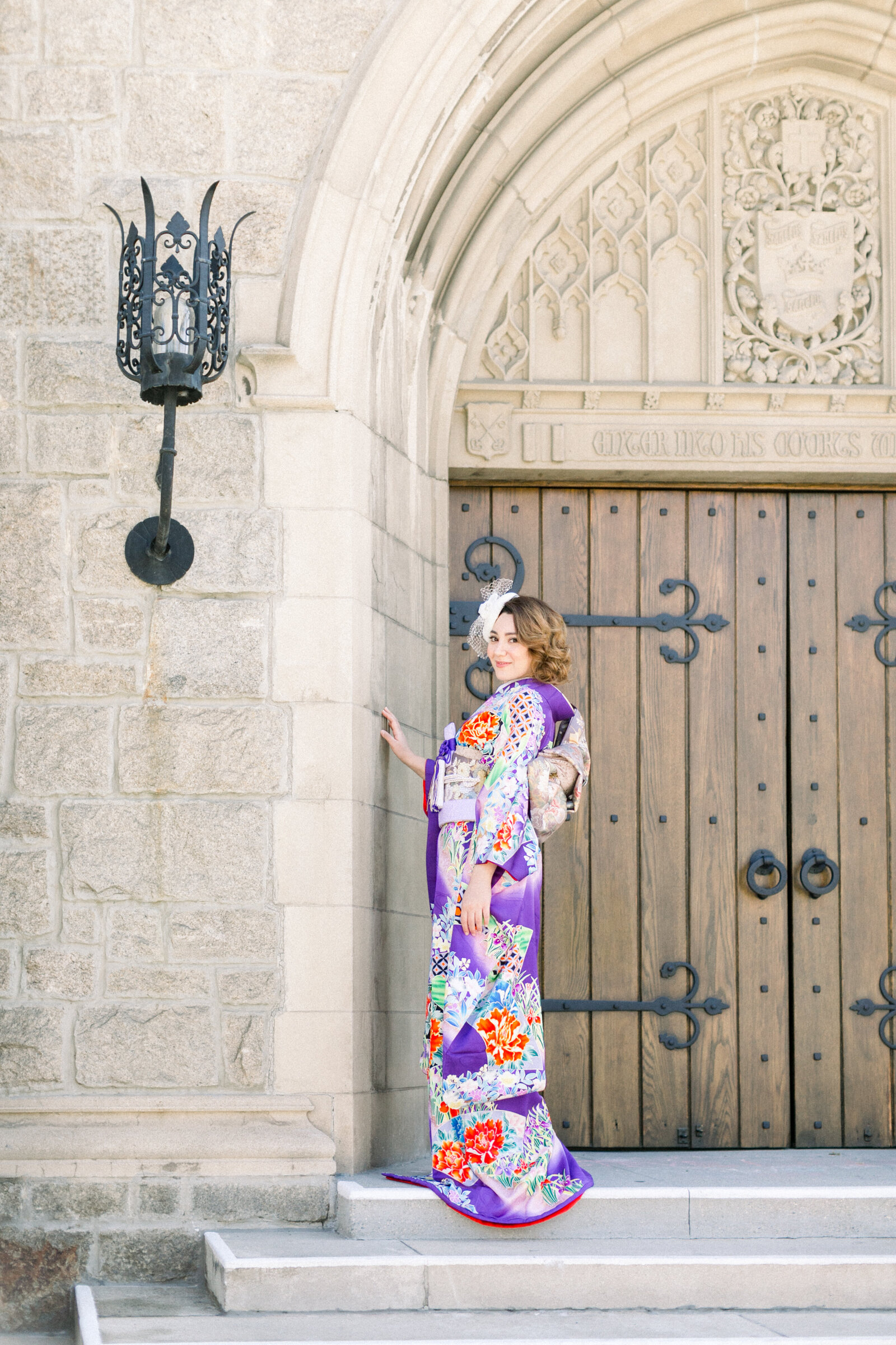 Bride in elegant purple floral wedding kimono rental standing by the grand wooden doorway of All Saints Episcopal Church, Pasadena Los Angeles | オールセインツ教会 紫色花柄振袖の花嫁 重厚な扉前での着物レンタルウェディング