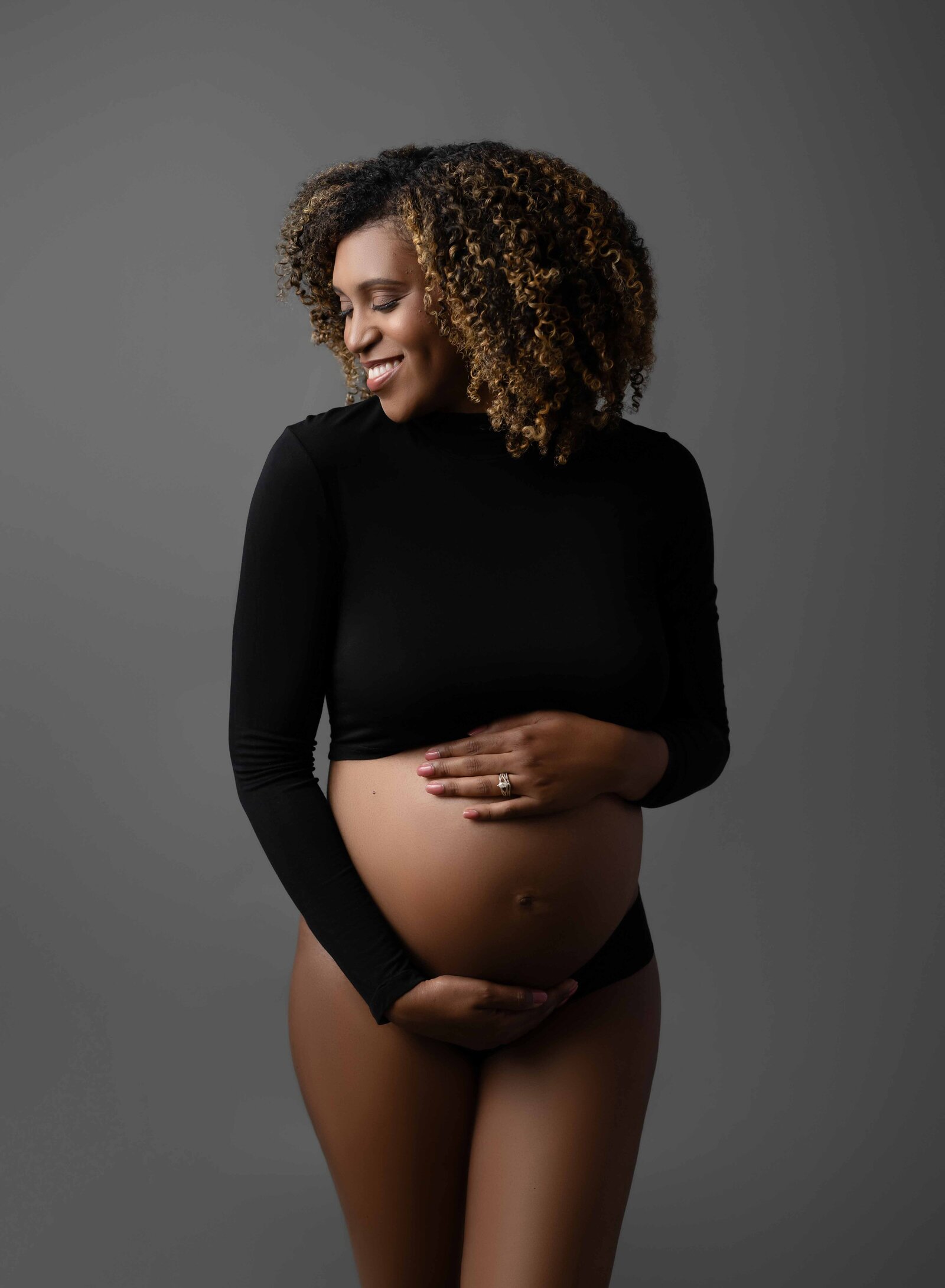 Pregnant women in black crop top smiling and holding her baby bump. Photo taken at Atlanta Maternity photo studio in Woodstock GA.