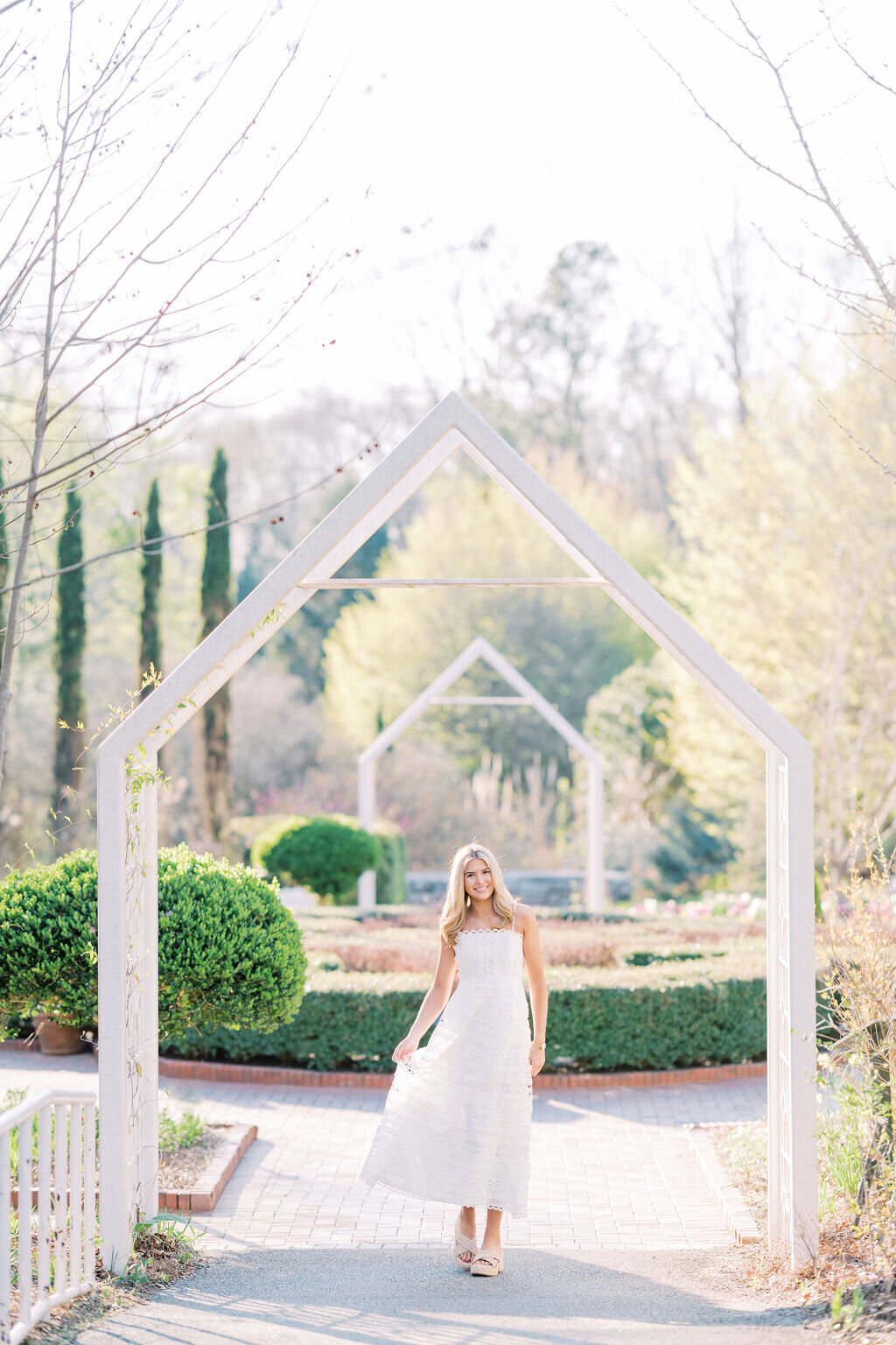 Girl stands under white pointed archway at the Athens botanical gardens
