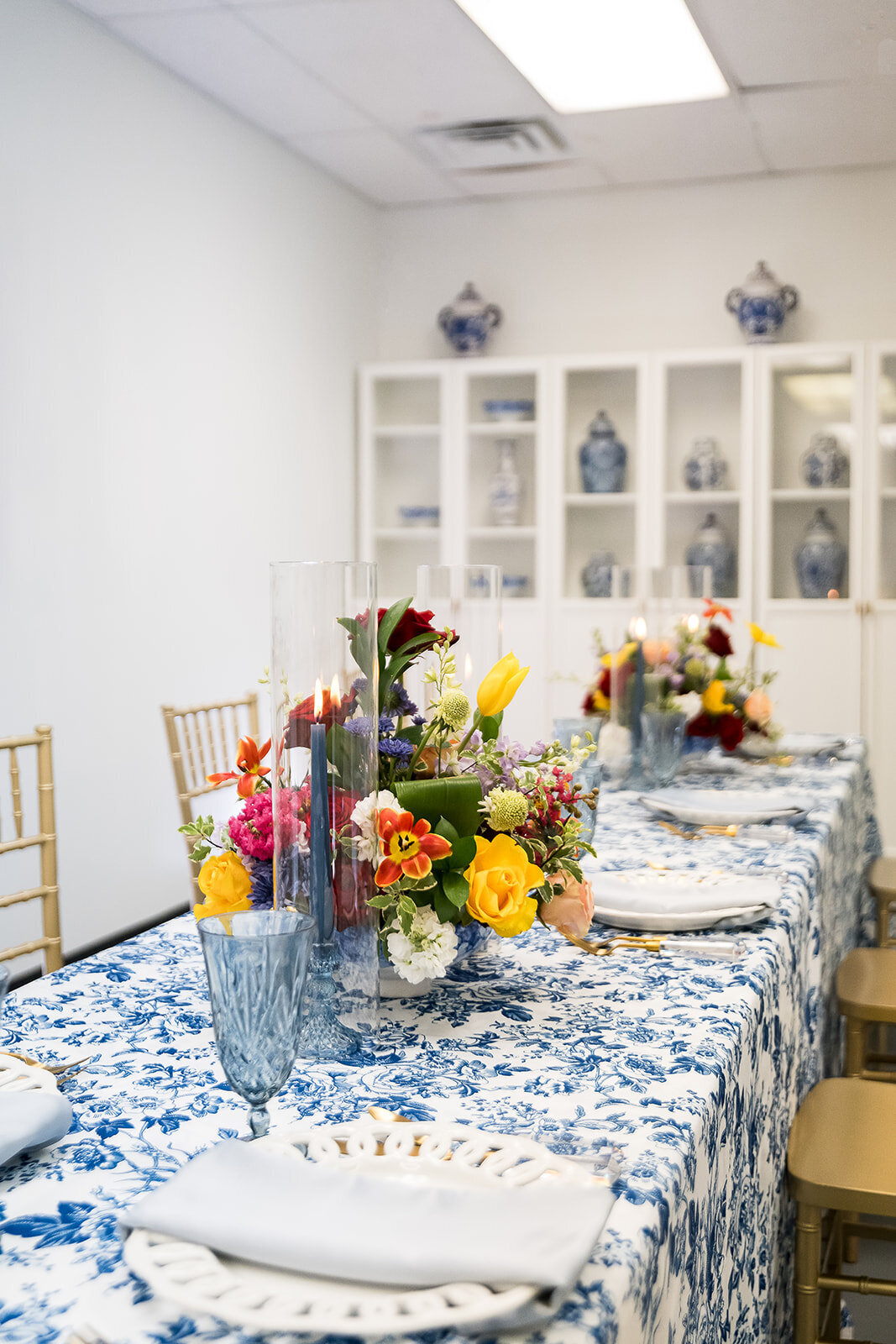 Styled table setup at The Parlor at Wells in Memphis, featuring vibrant floral centerpieces, blue toile linens, gold chairs, and natural light—ideal for showers, workshops, and private dinners.