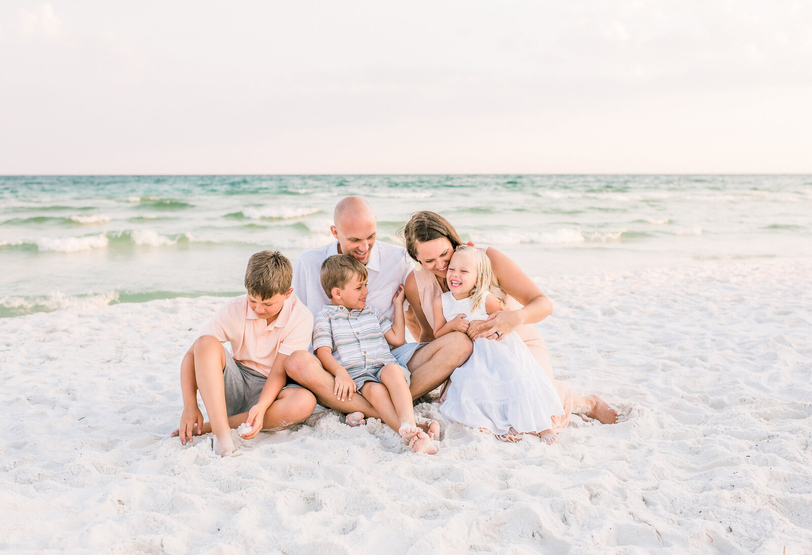 Family sitting on the white sand with the Gulf of Mexico in the background in Destin, FL