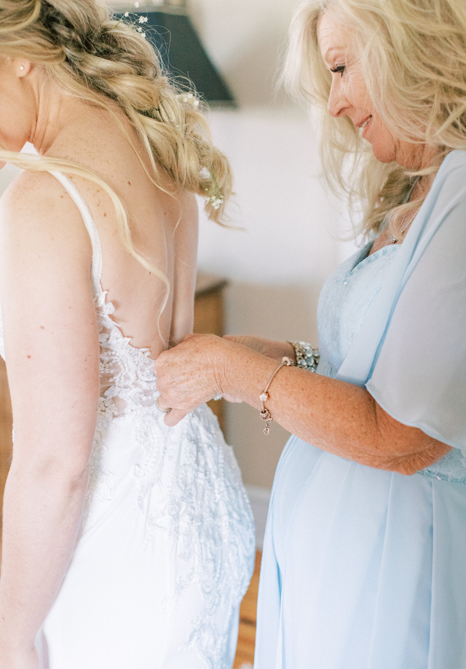 Bride has dress buttoned up by her mom