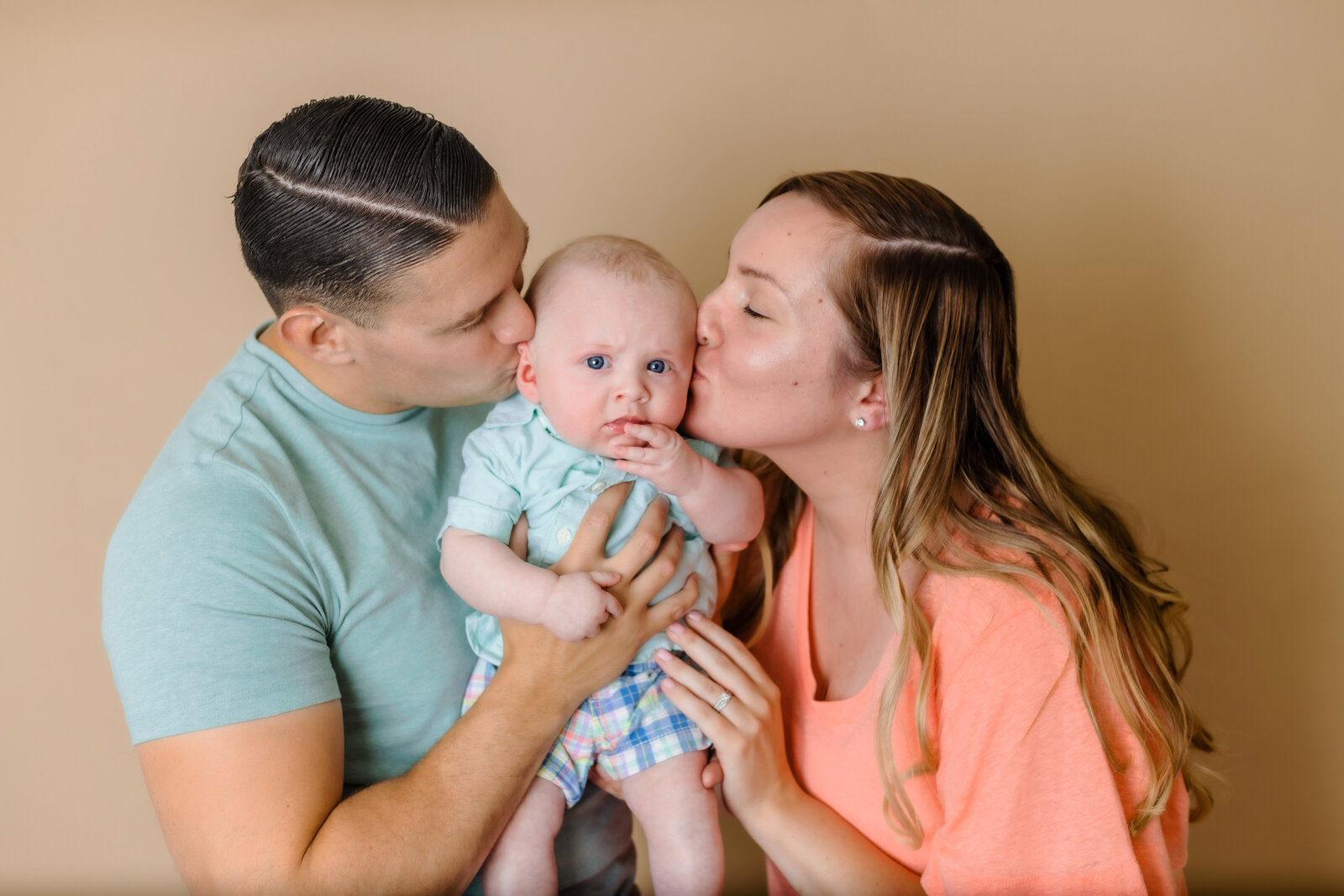 Milestone Photographer, a mother and father holds their baby boy up and kiss him