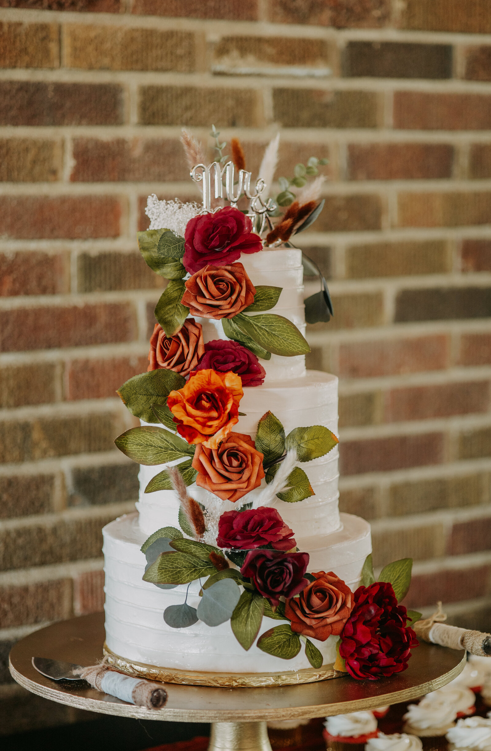 Wedding cake adorned with fall-colored flowers, forming a swoop down the side for a beautiful, seasonal touch.