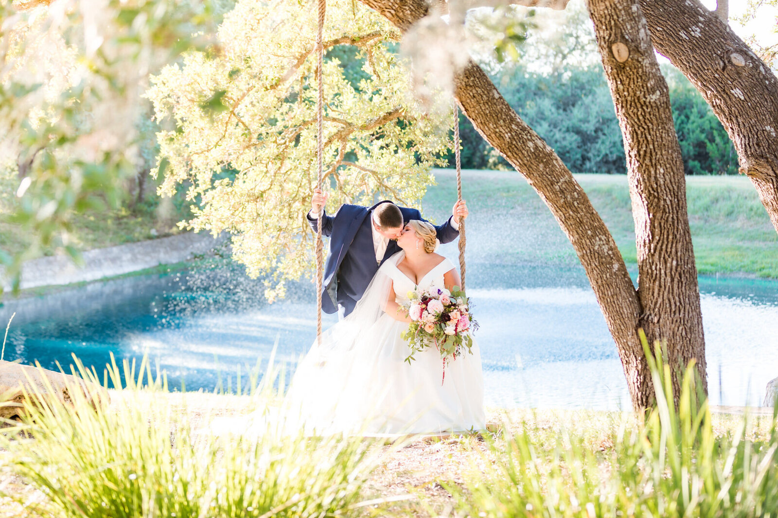 A bride and groom kiss on the tree swing.