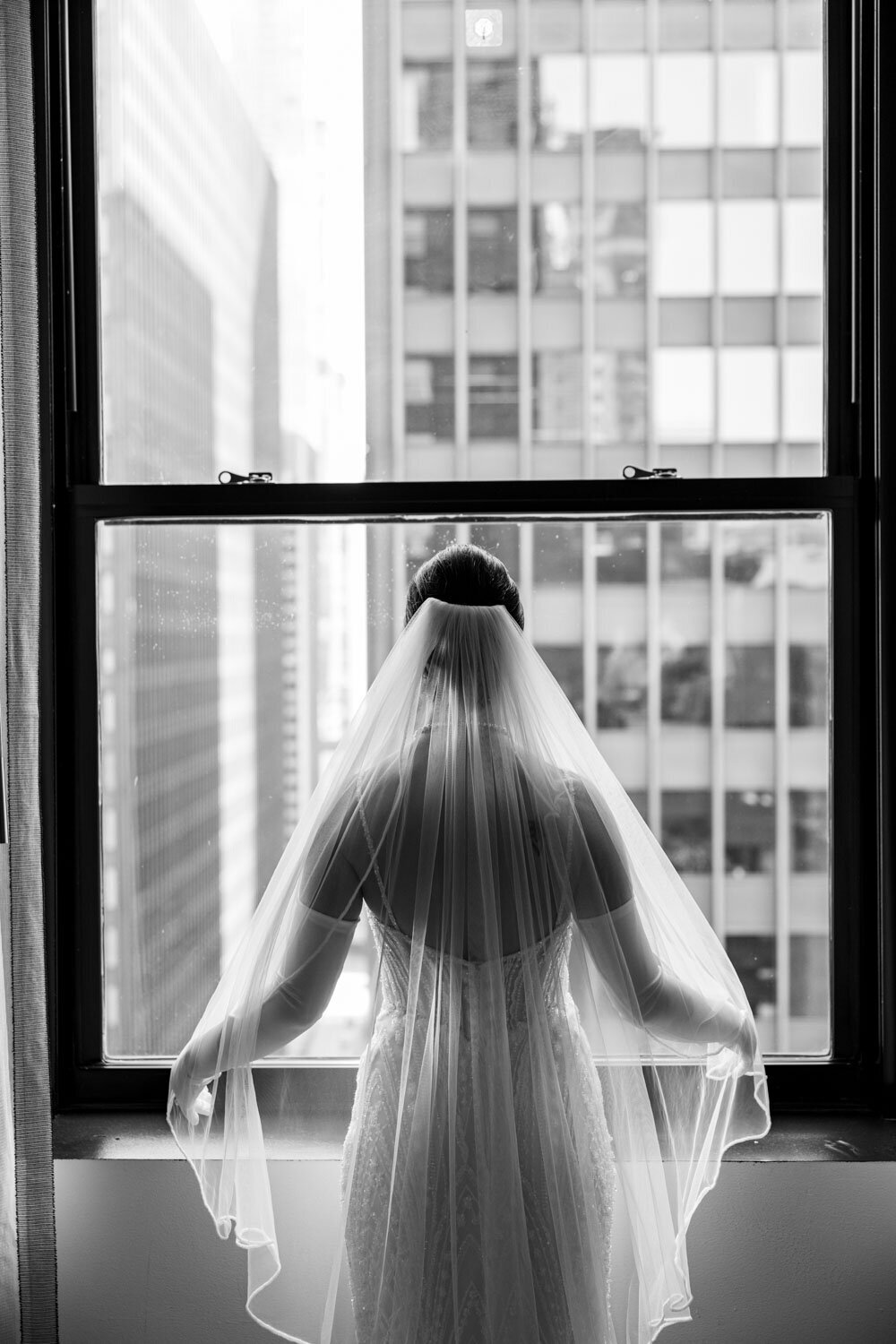 A woman in a wedding dress and veil looks out a window