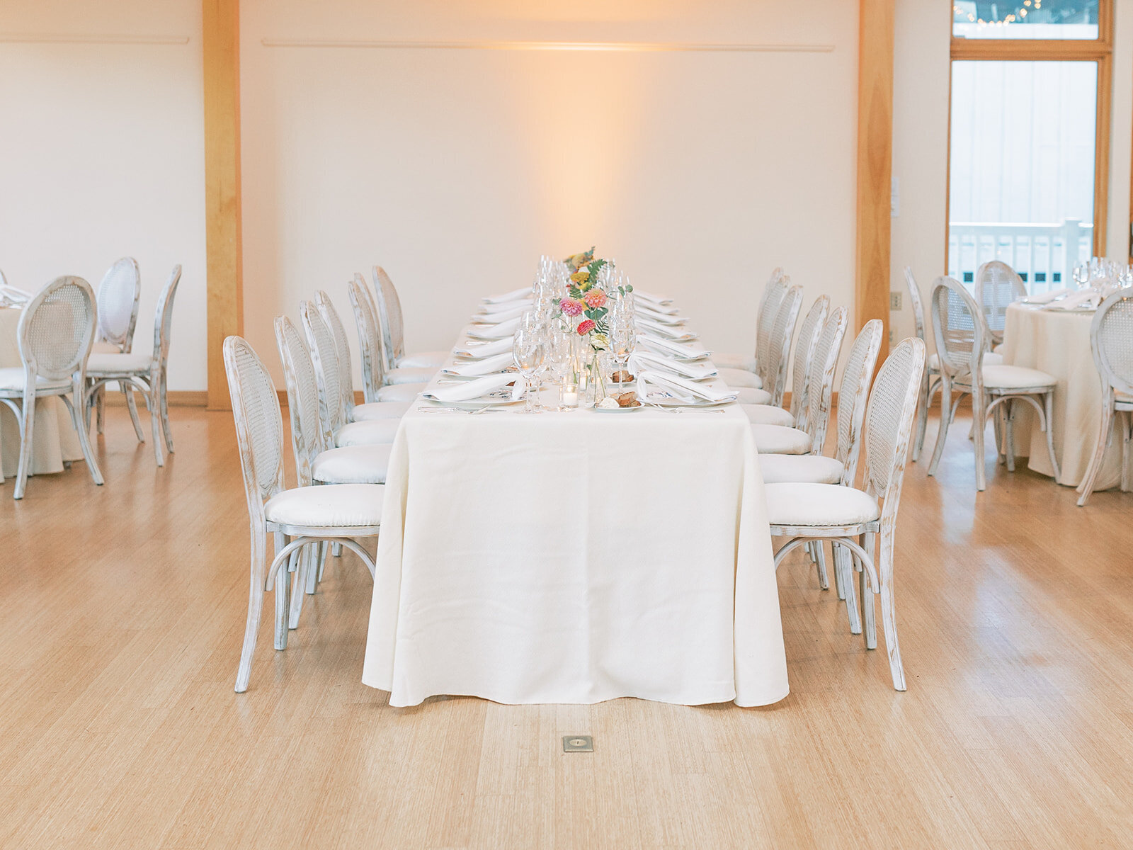 a long white table with white chairs at an indoor wedding reception