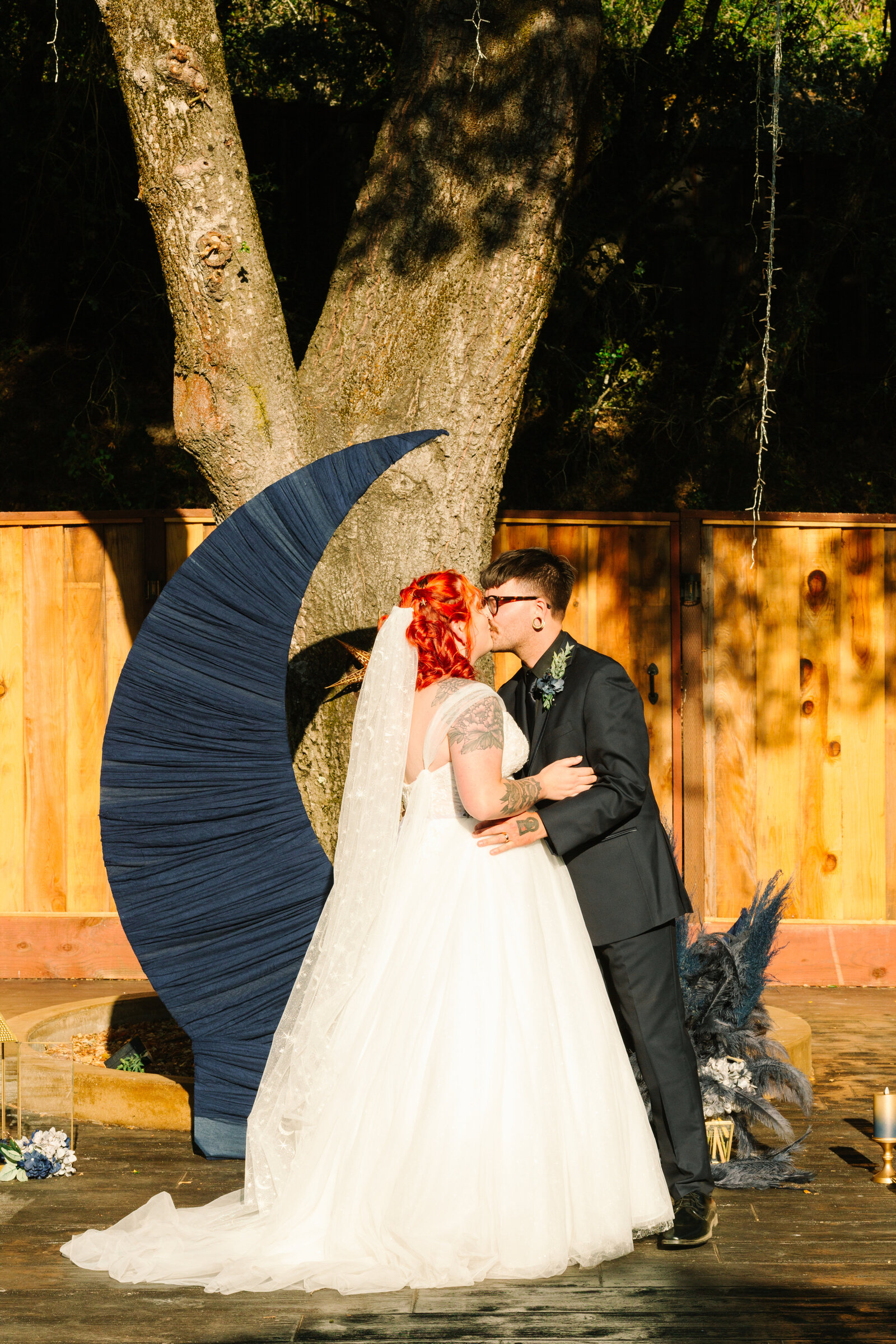 First kiss of a backyard wedding with a tattooed bride and groom.