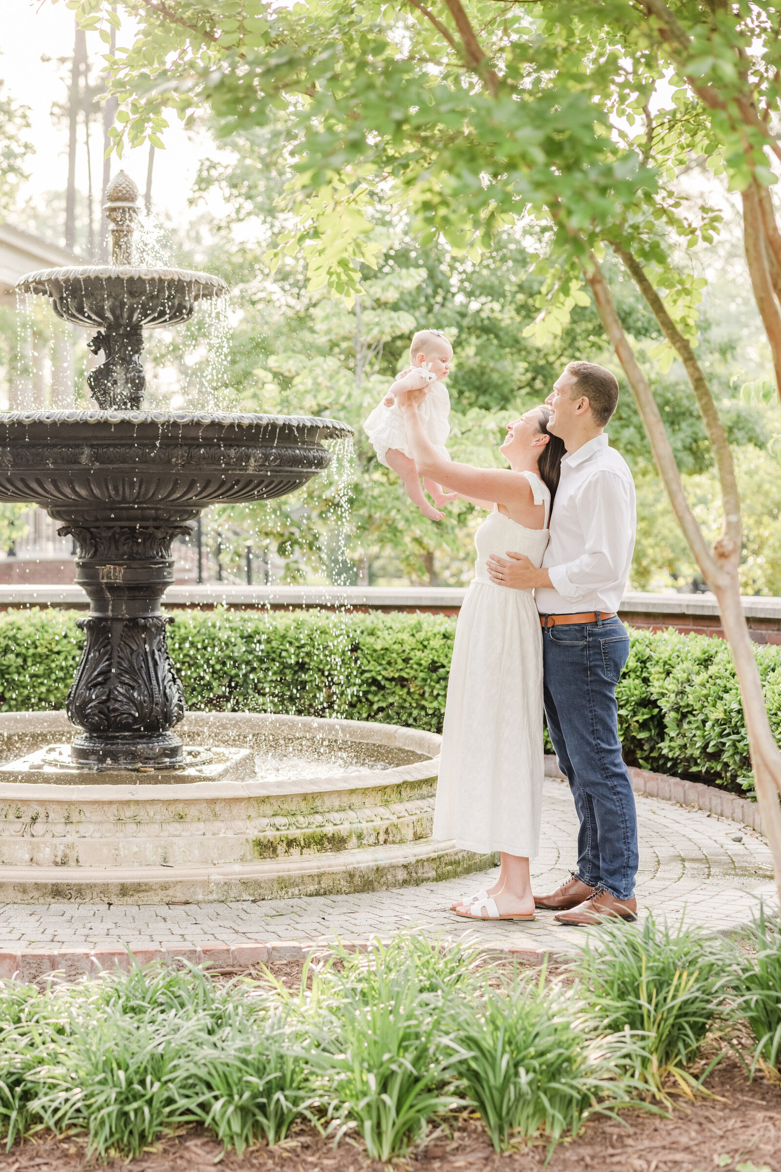 Parents holding up their baby by an elegant fountain.