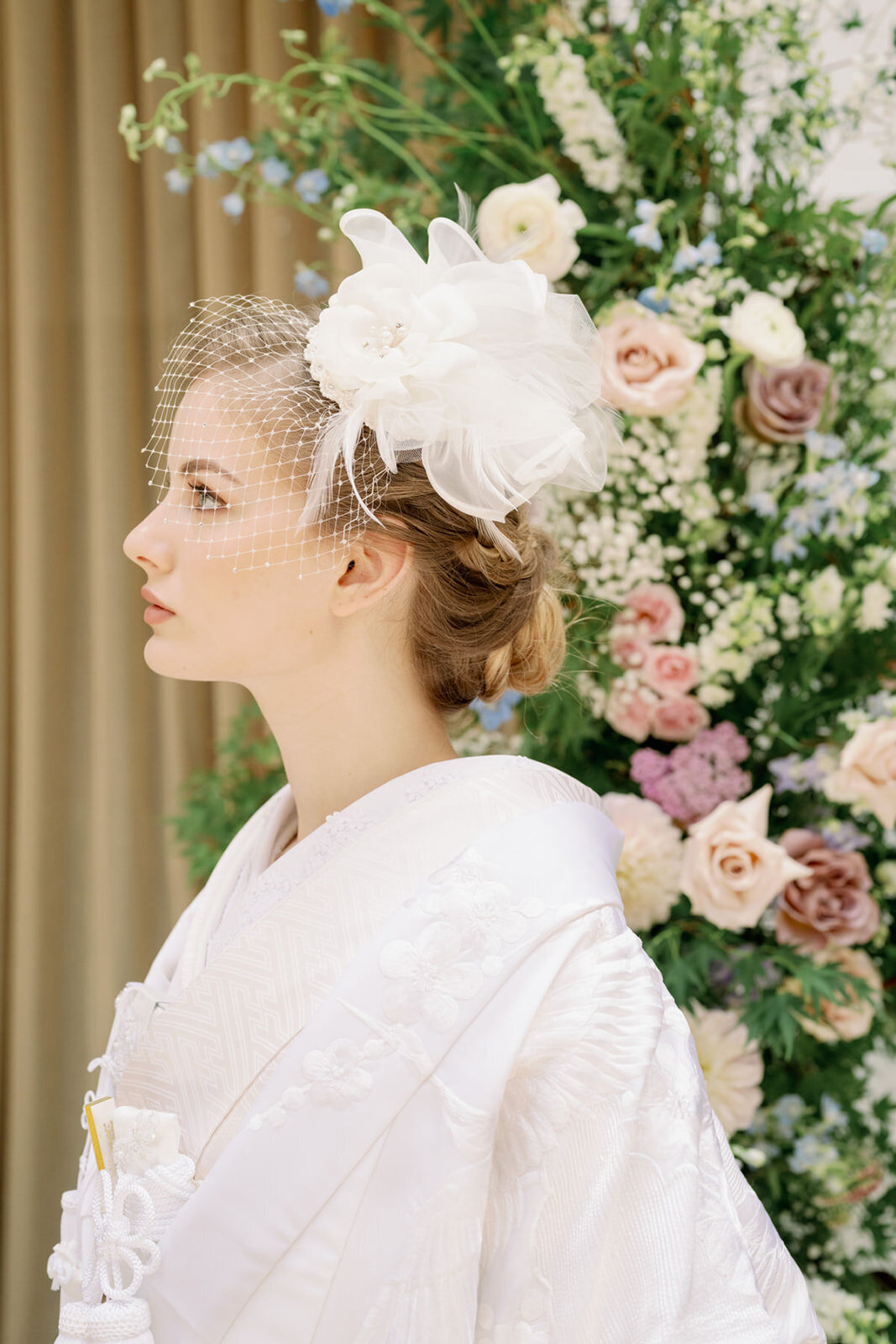 Bride wearing shiromuku (白無垢) wedding kimono in a traditional Japanese wedding ceremony with floral background.