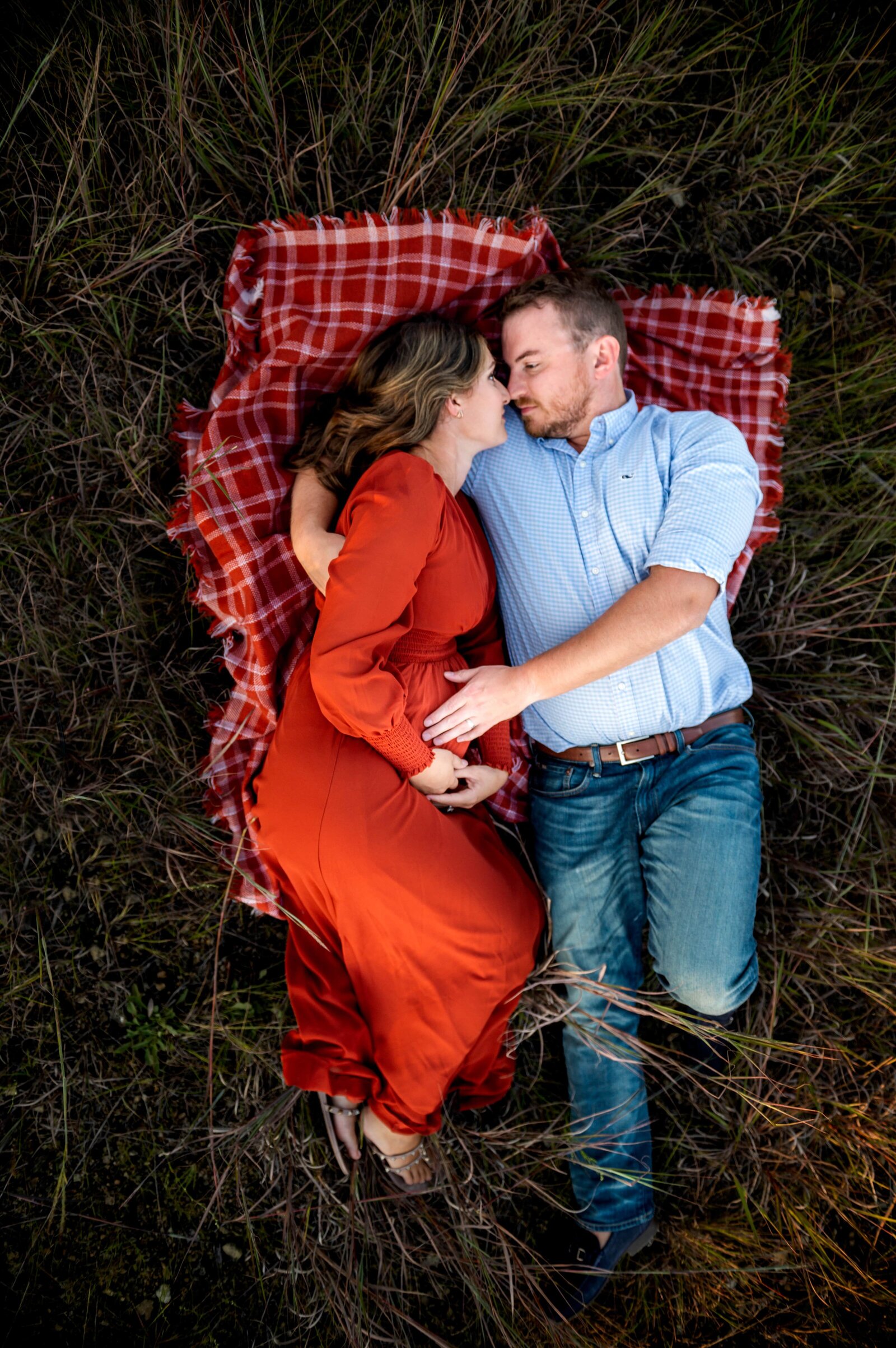 pregnant couple laying in a field  holding eachother