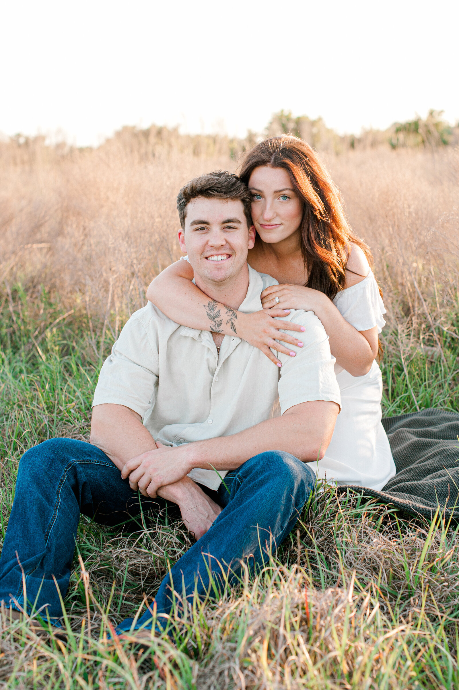 Couple sitting in a tall grass field smile at the camera for a close up portrait