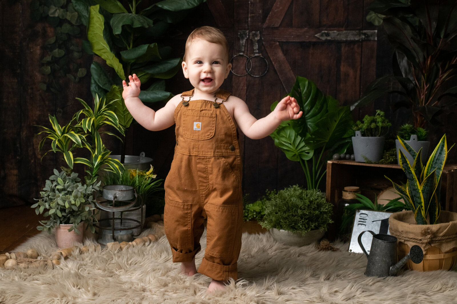 happy baby in overalls in greenhouse set