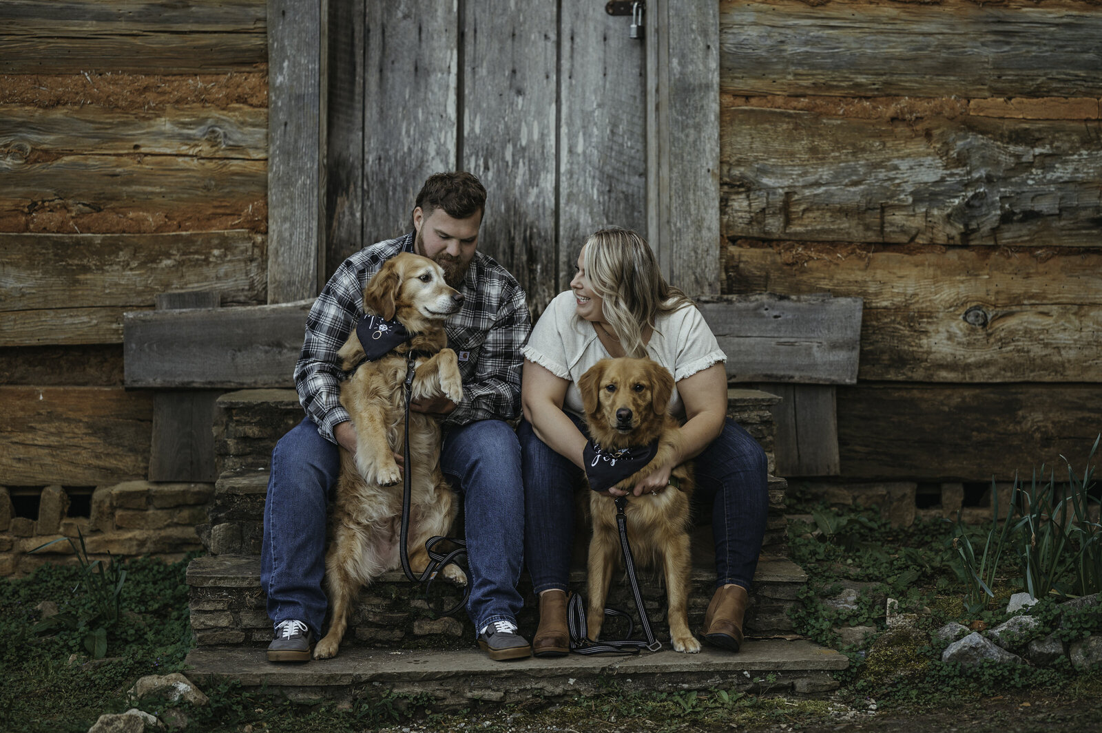 Engaged couple sit on steps while playing with their two golden retriever dogs. Photo taken at Fort Yargo State Park.