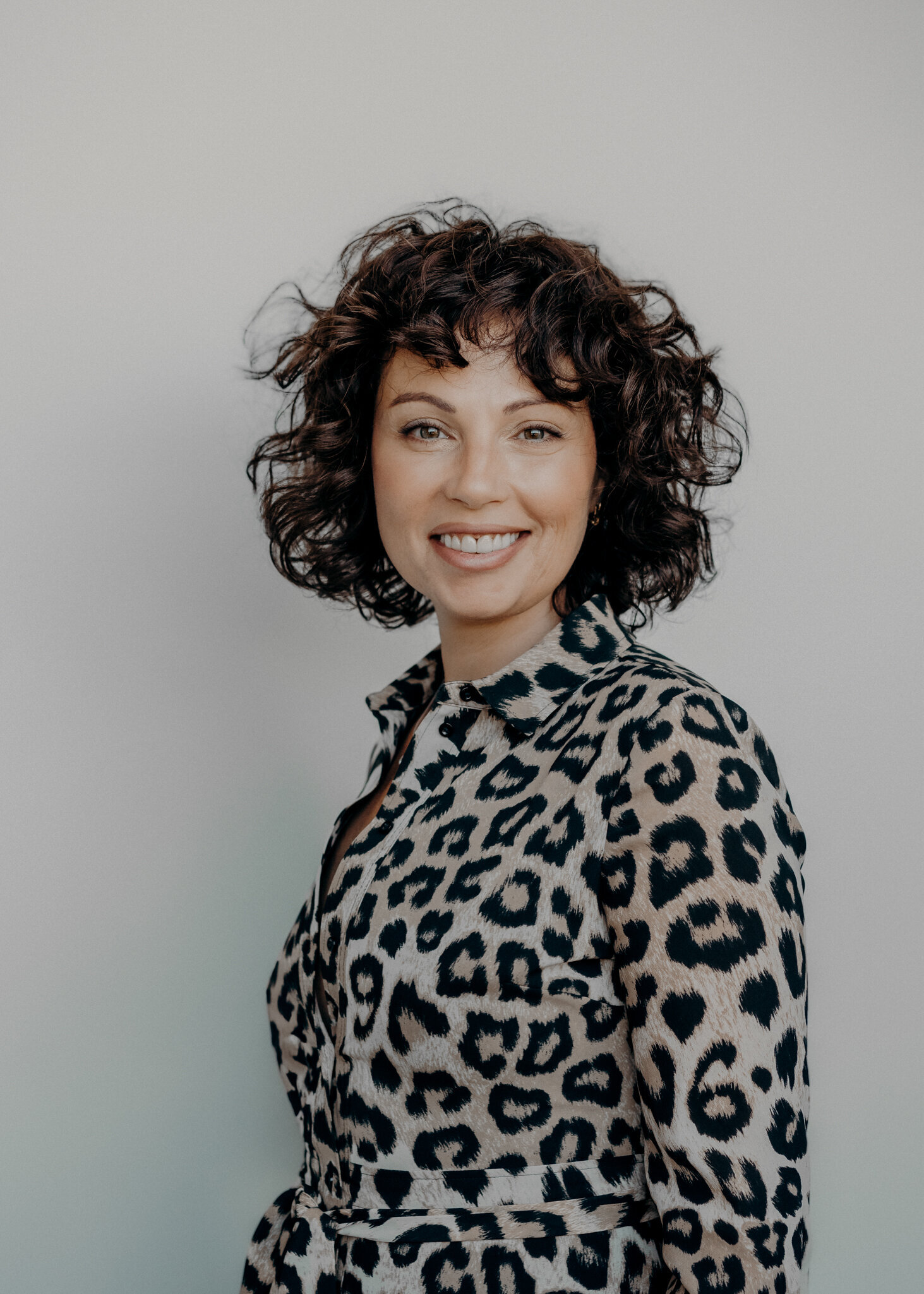 A stunning woman wears a leopard print shirt with her short curly hair during her personal branding session for her real estate company in Denver.