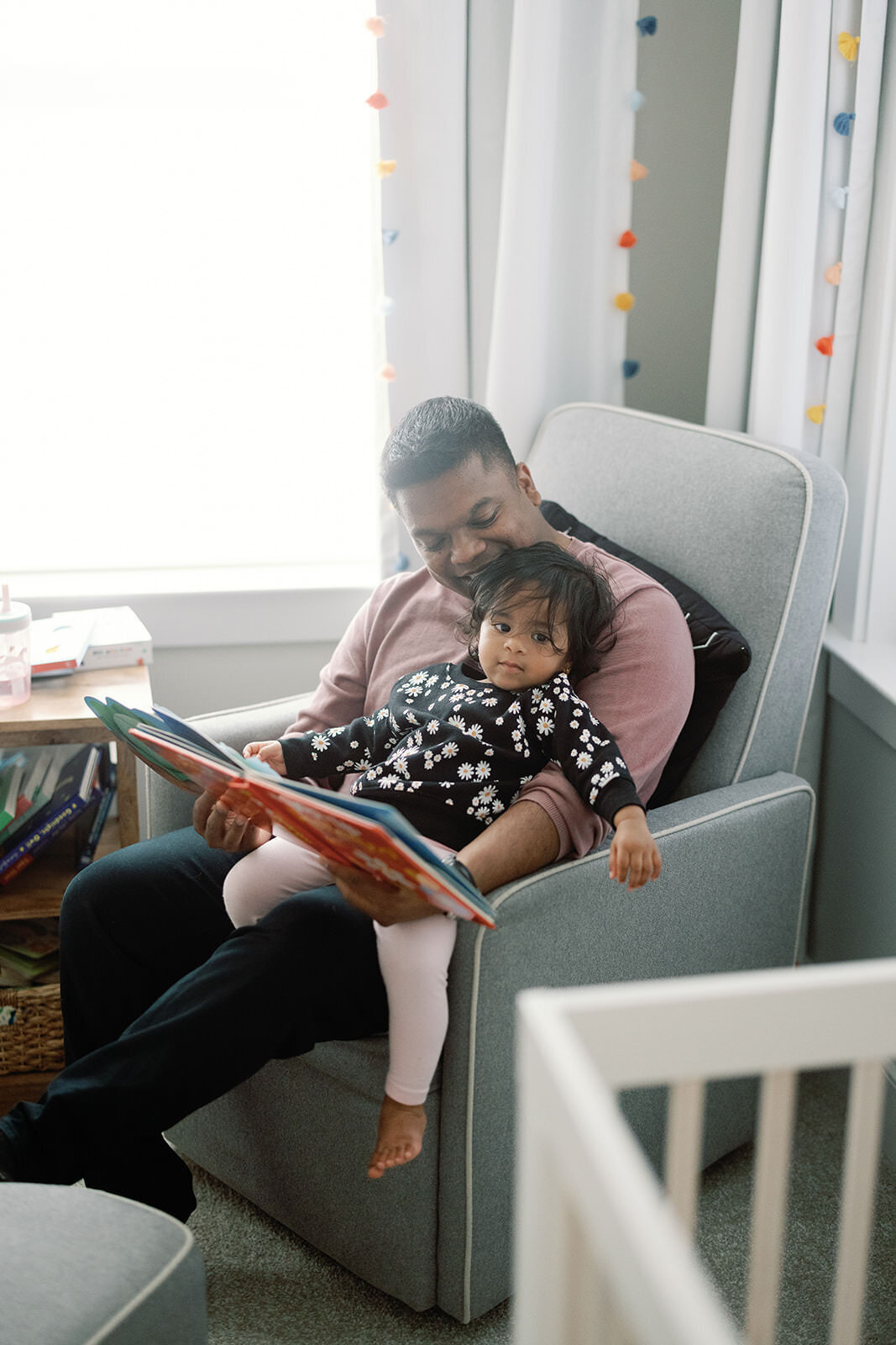 Intimate father-daughter moment, with the father reading a book to his toddler in a cozy nursery setting.