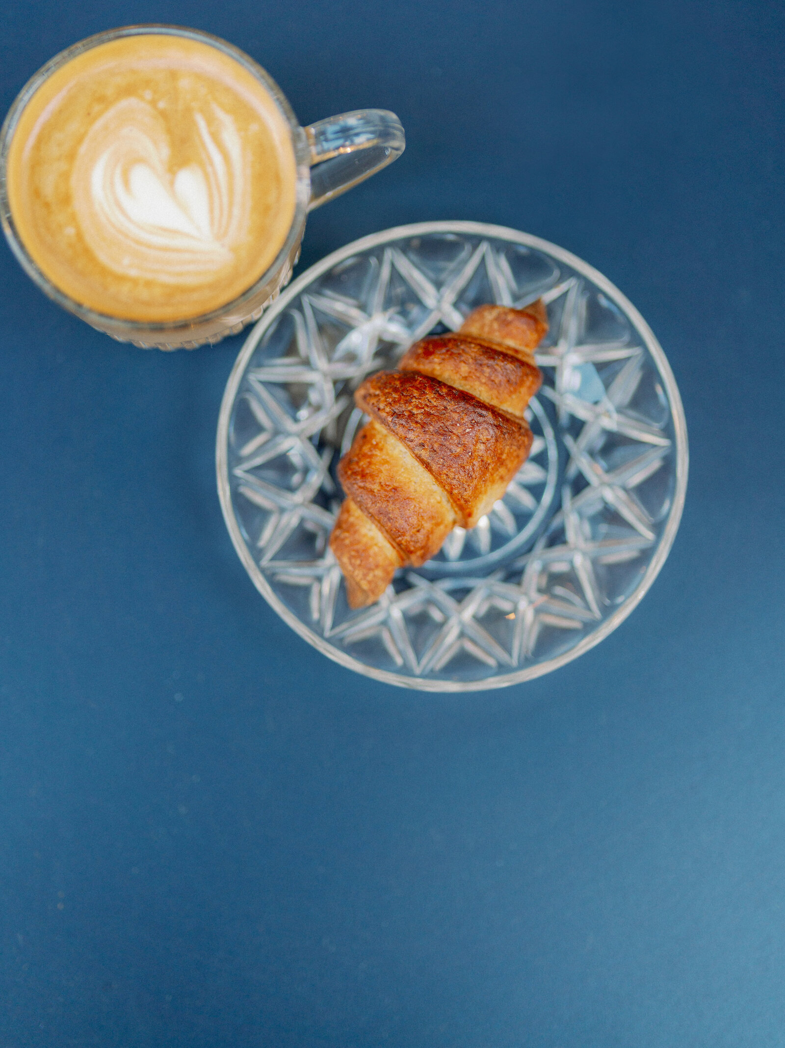 a blue table with coffee and croissant  on a clear plate